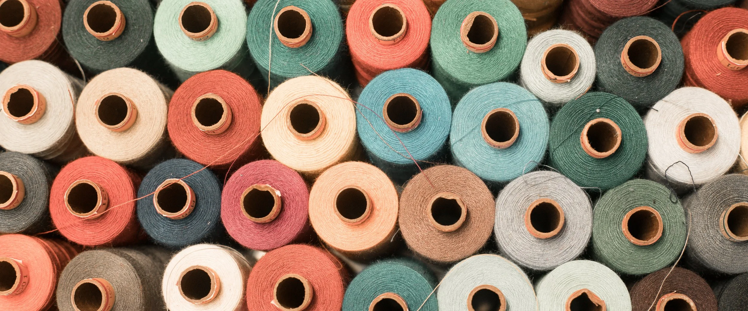 Multiple spools of thread in various colors including red, green, white, gray, peach, blue, and black.
