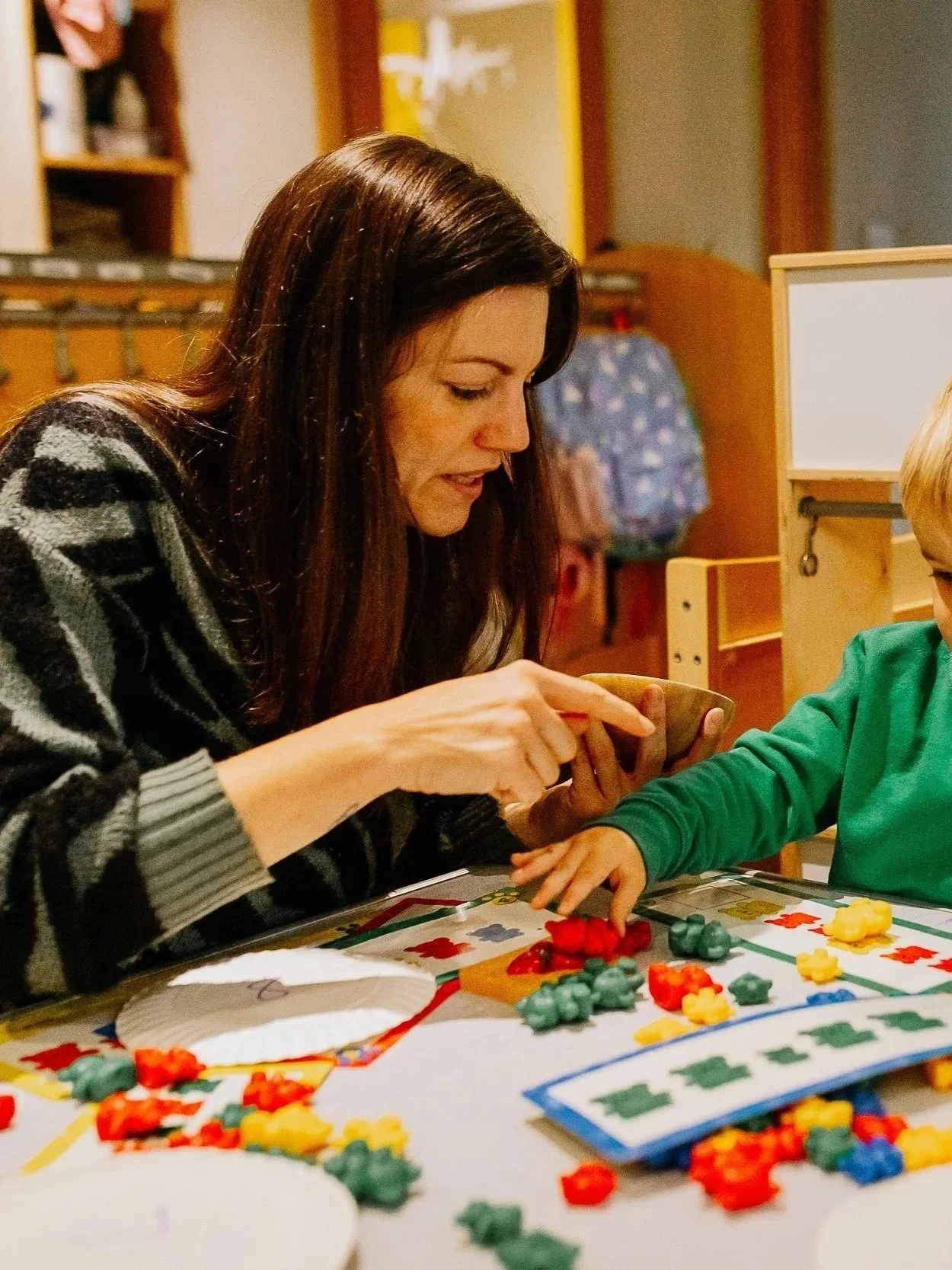 A woman and a young boy sitting at a table playing a board game with colorful game pieces.