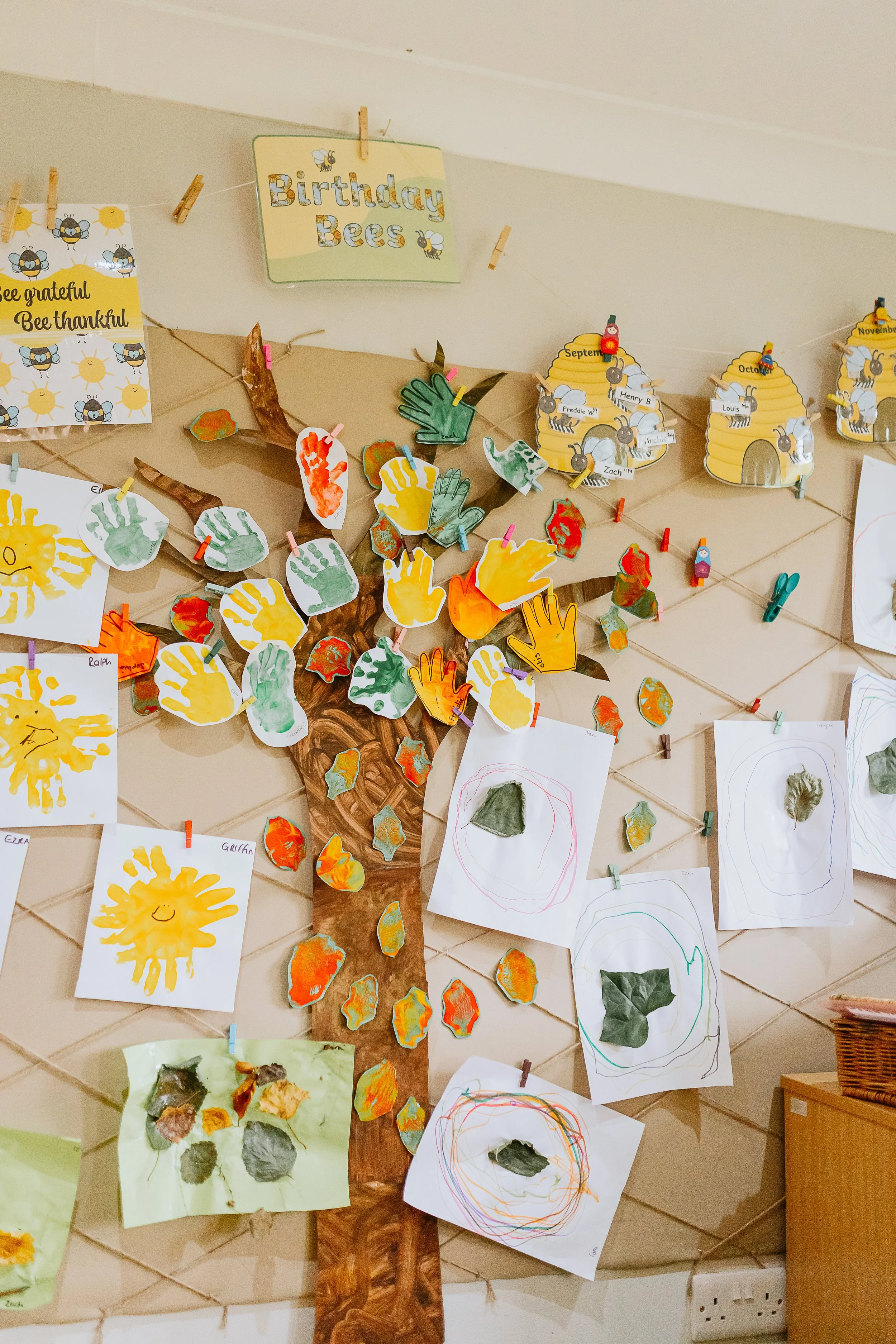 A wall display featuring children's artwork related to bees, including drawings of bees, beehives, and handprint art, along with signs that say 'Birthday Bees' and motivational phrases about bees.