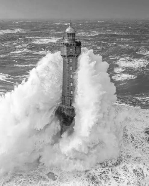 een vuurtoren op een rots ondergedompeld door grote golven in een ruige oceaan