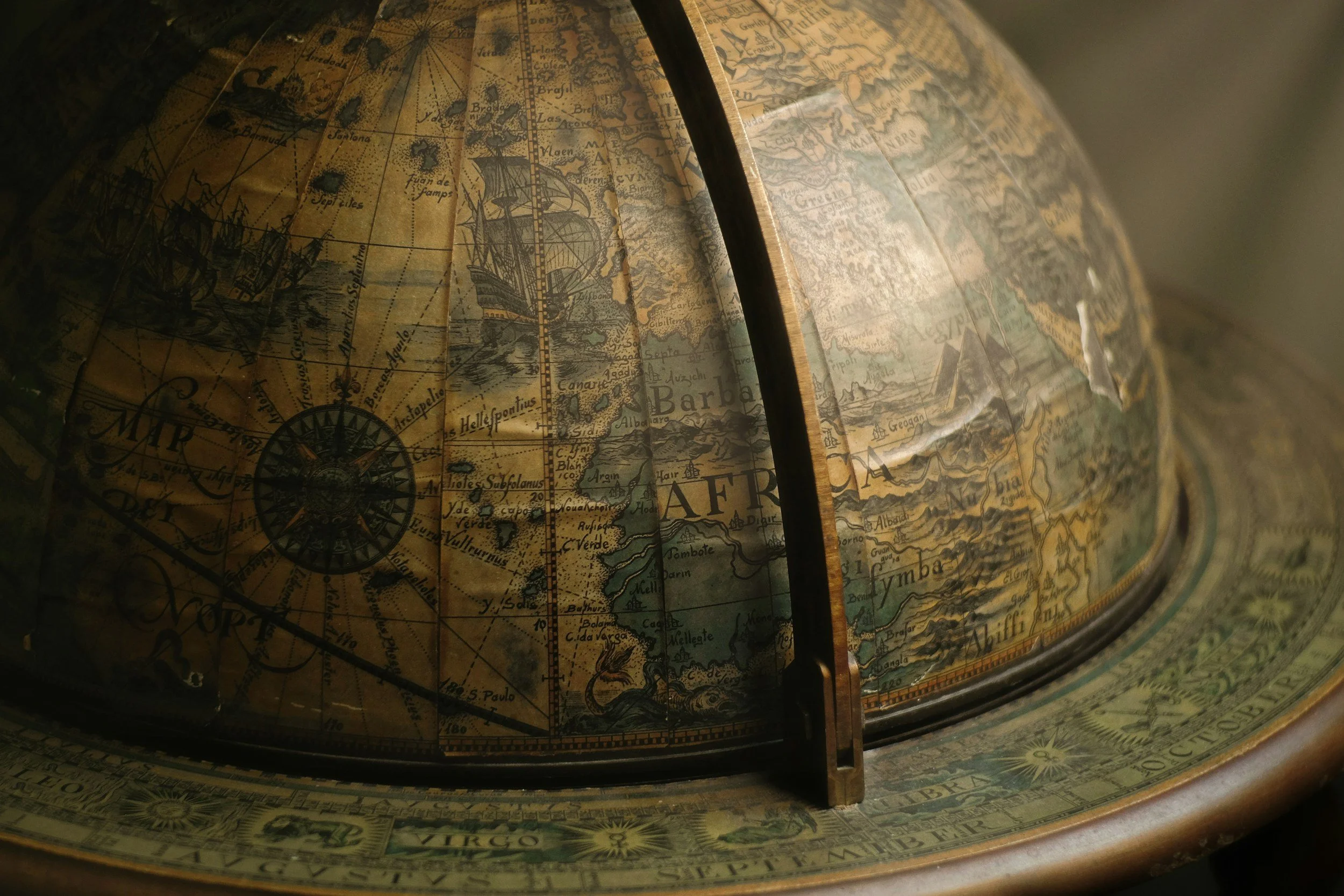Close-up of an antique celestial globe showing map details and compass roses with a vertical metal arm dividing the globe into sections
