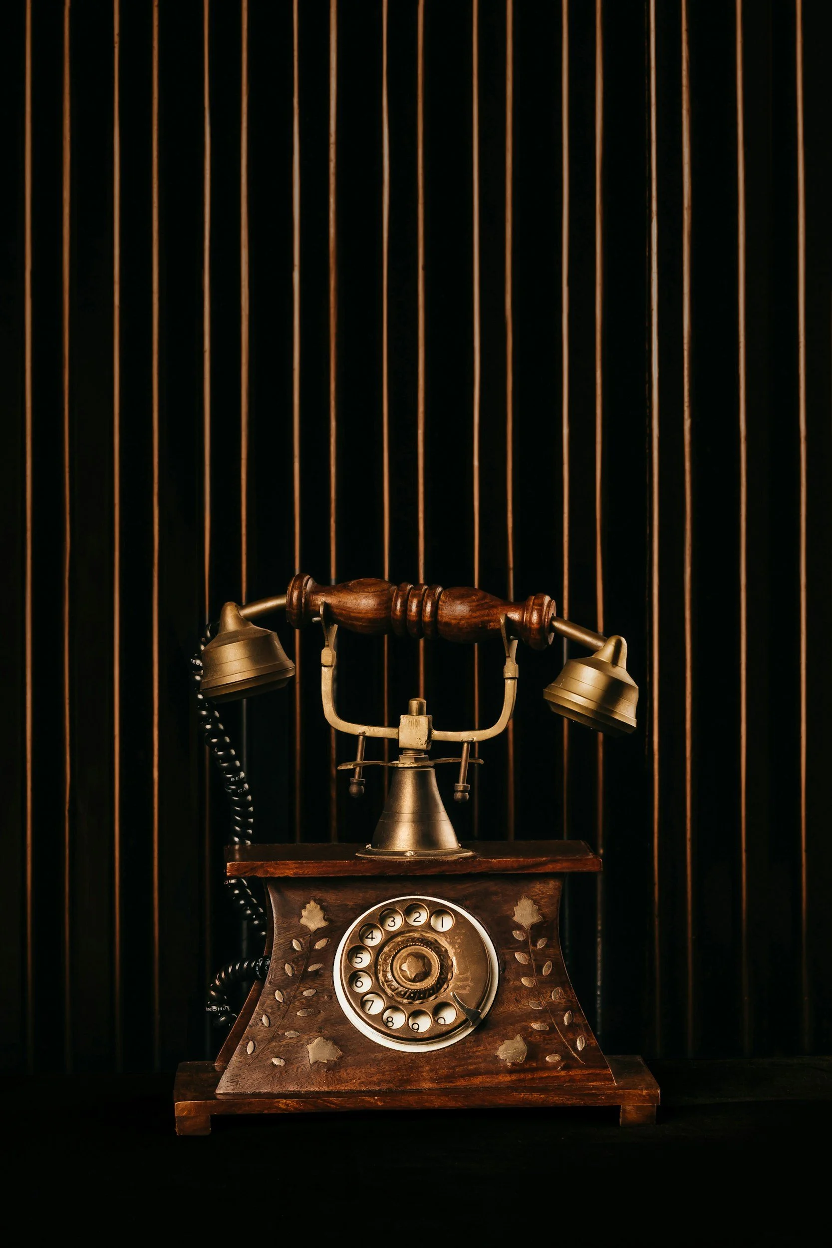 Vintage rotary telephone with a wooden handle and brass accents on a dark surface, against a black background with vertical gold lines.
