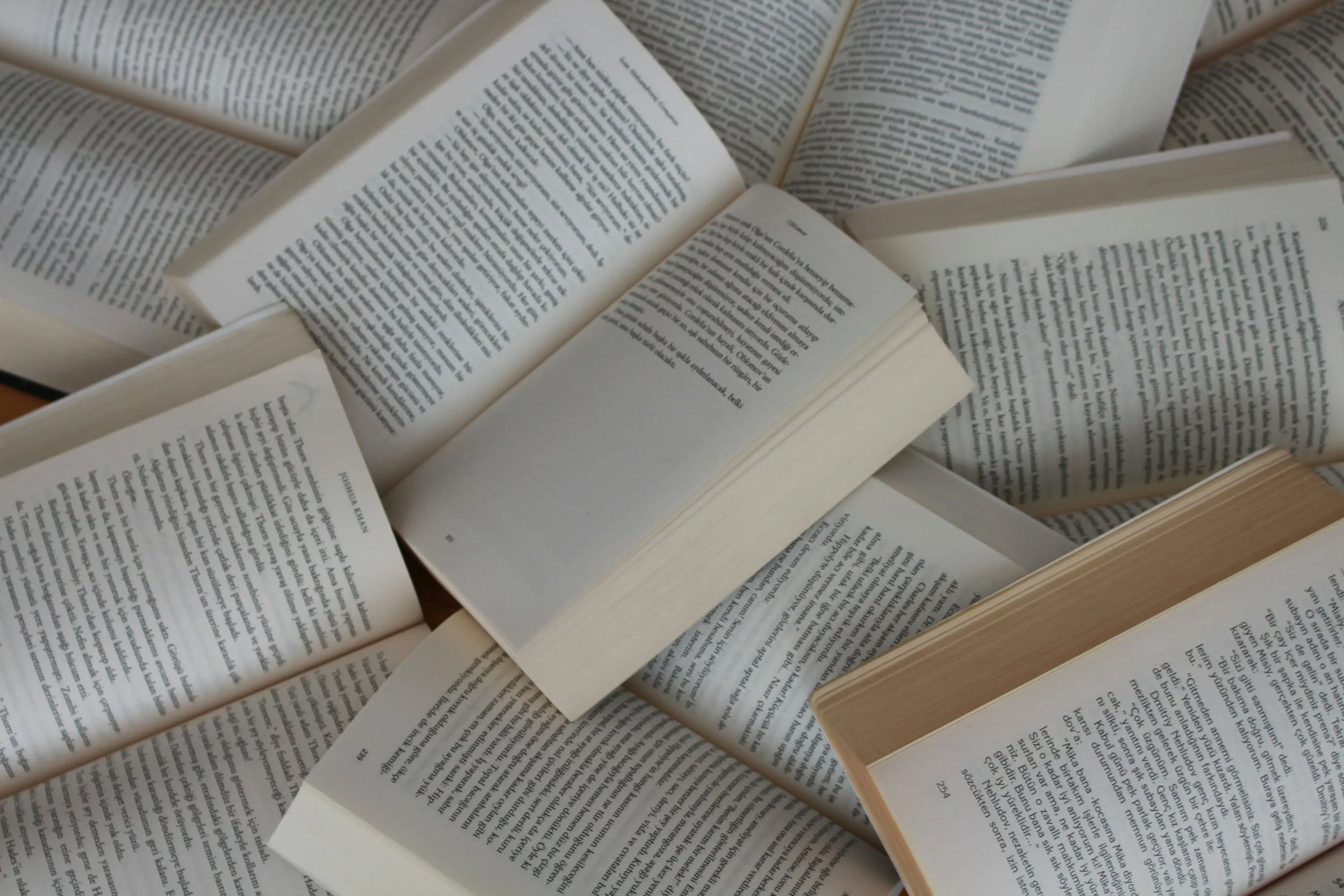 Several open books with pages spread out on a flat surface, displaying text.