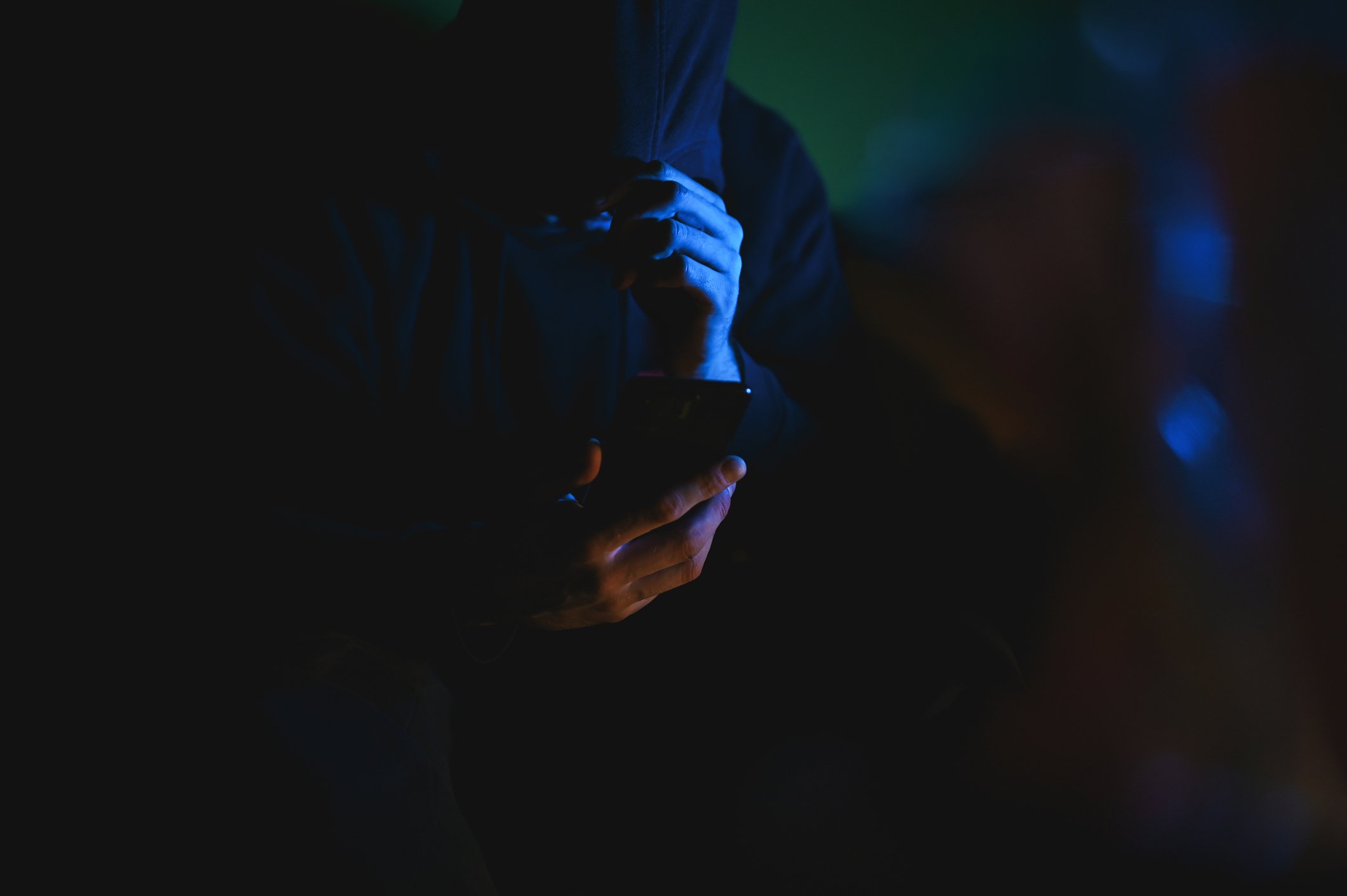 Person in dunklem Raum schaut auf Smartphone, mit blauer Beleuchtung