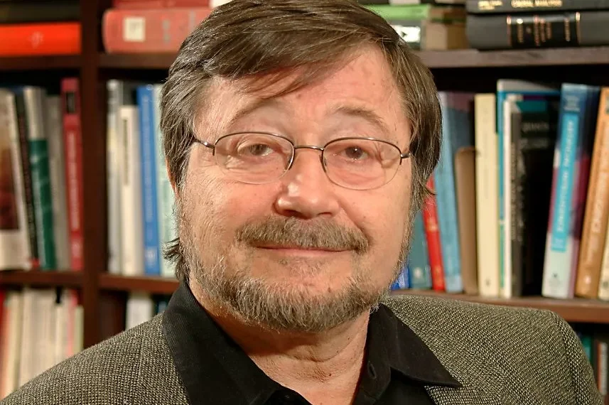 Ein Mann mit Brille, grauem Haar und Bart, vor einer Bücherwand.