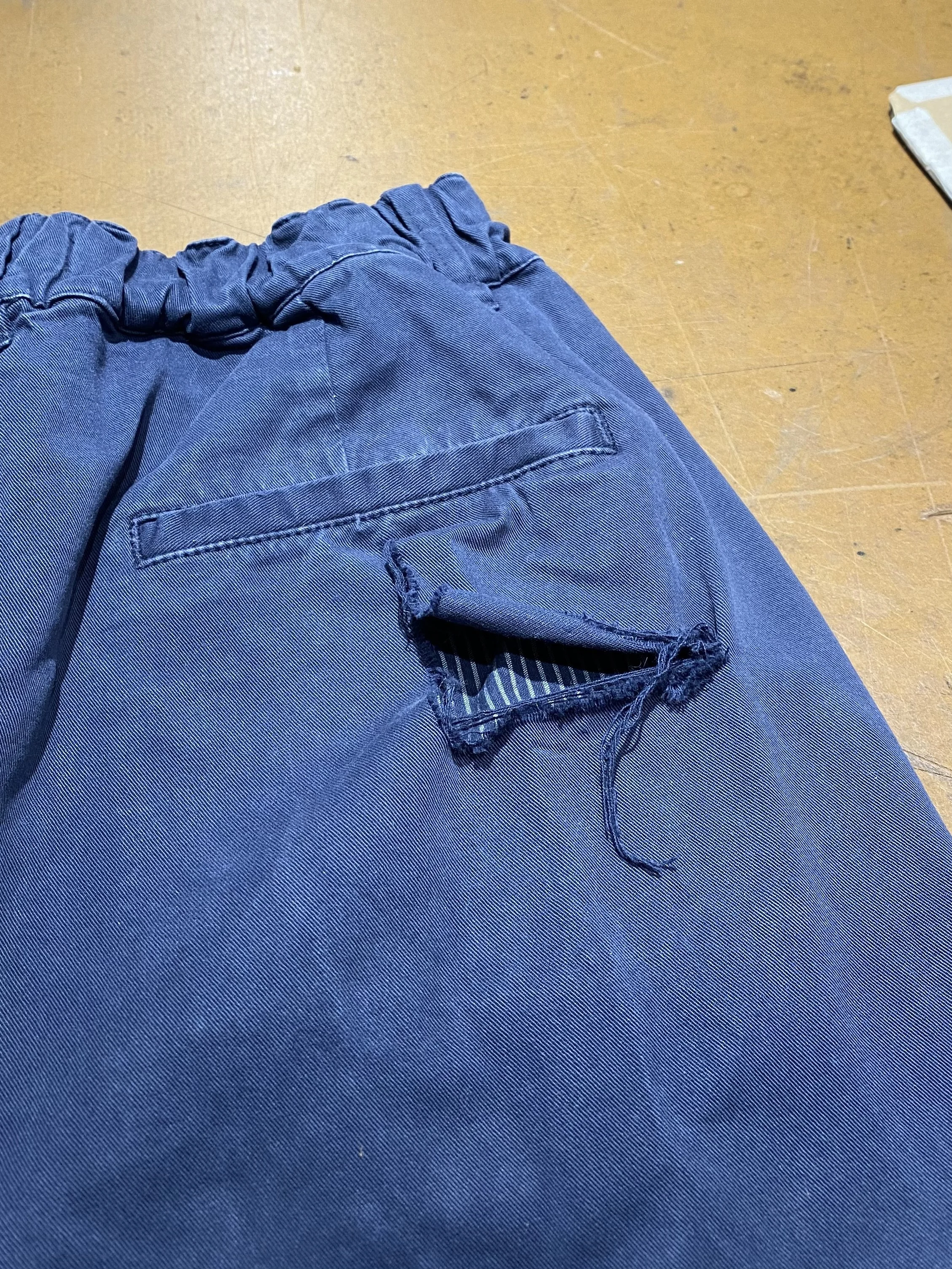 Tear at seat pocket of navy cotton trousers
