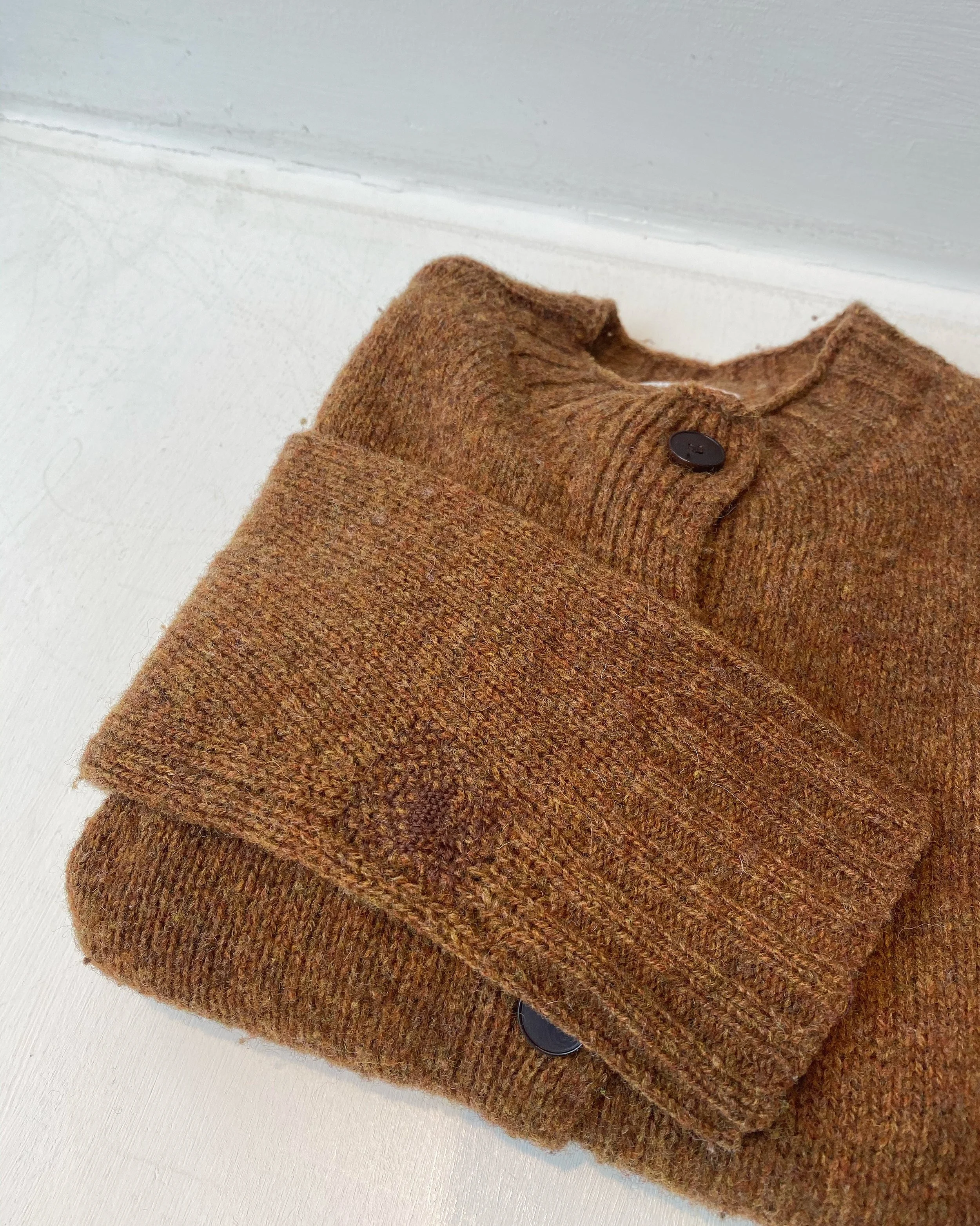 Discreet darn on knitted cardigan: Small hole on sleeve of cinnamon coloured knitted cardigan, repaired using woven darning in close matching wool.
