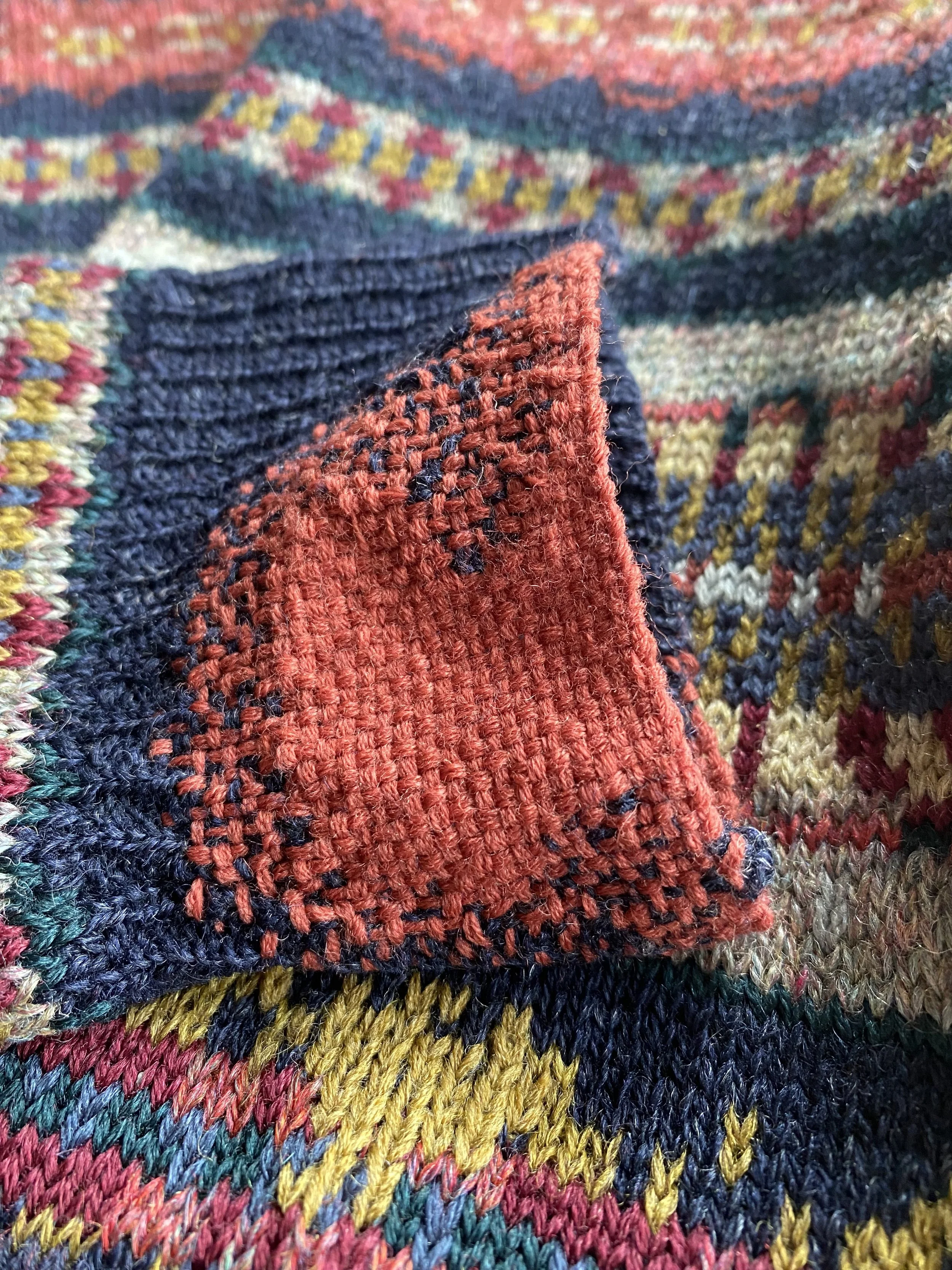 Visible mended cuff using woven darning in rusty red coloured mending yarn