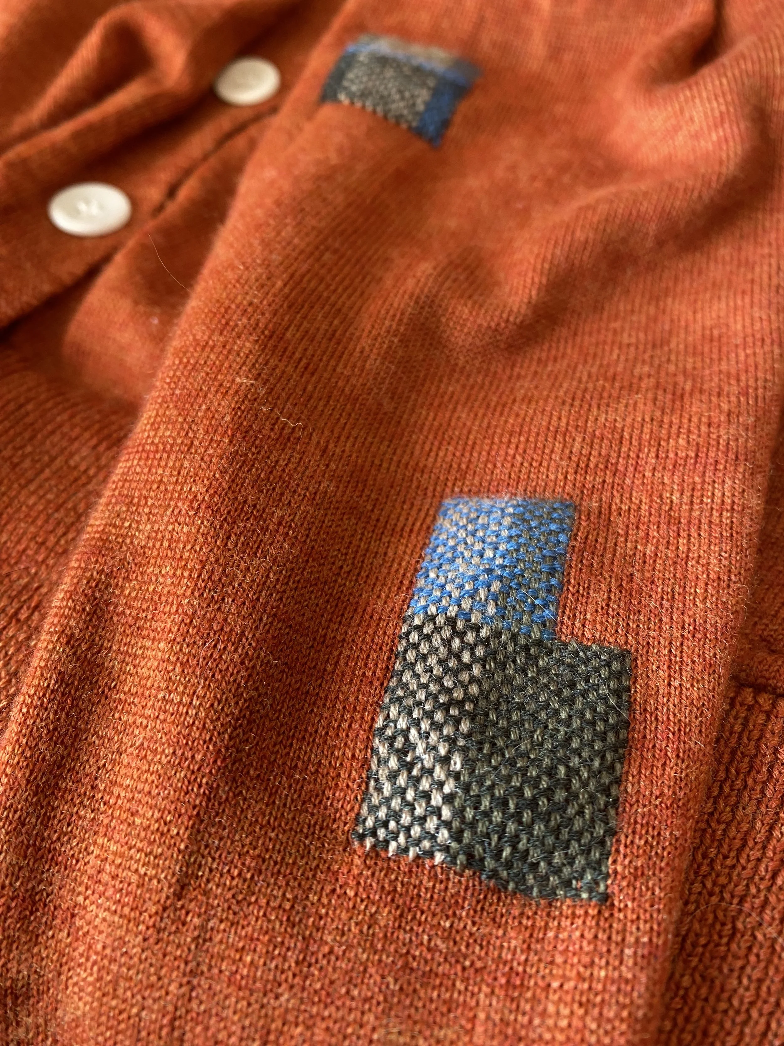 Visible repair on knitwear: Visible woven darn in greens and light blue grid pattern and block shape on a lightweight orange knit.
