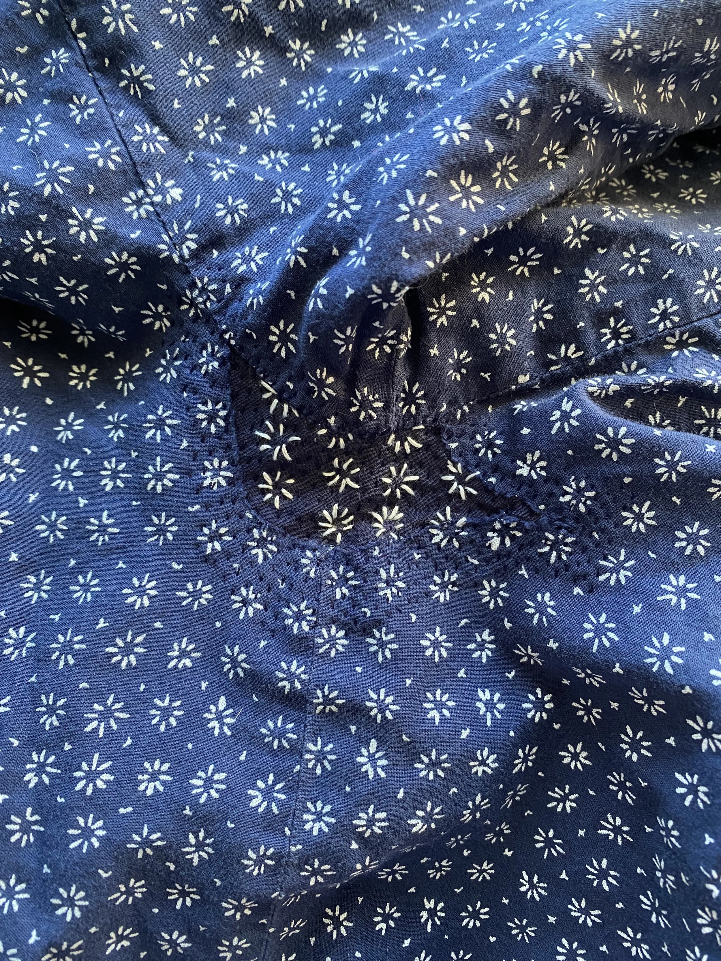 Invisible repair on night dress: Navy fabric with white print of small daisy like shapes, repaired with navy patch on inside and stitched in place with matching navy thread and white thread added to mimic pattern across new patched area.