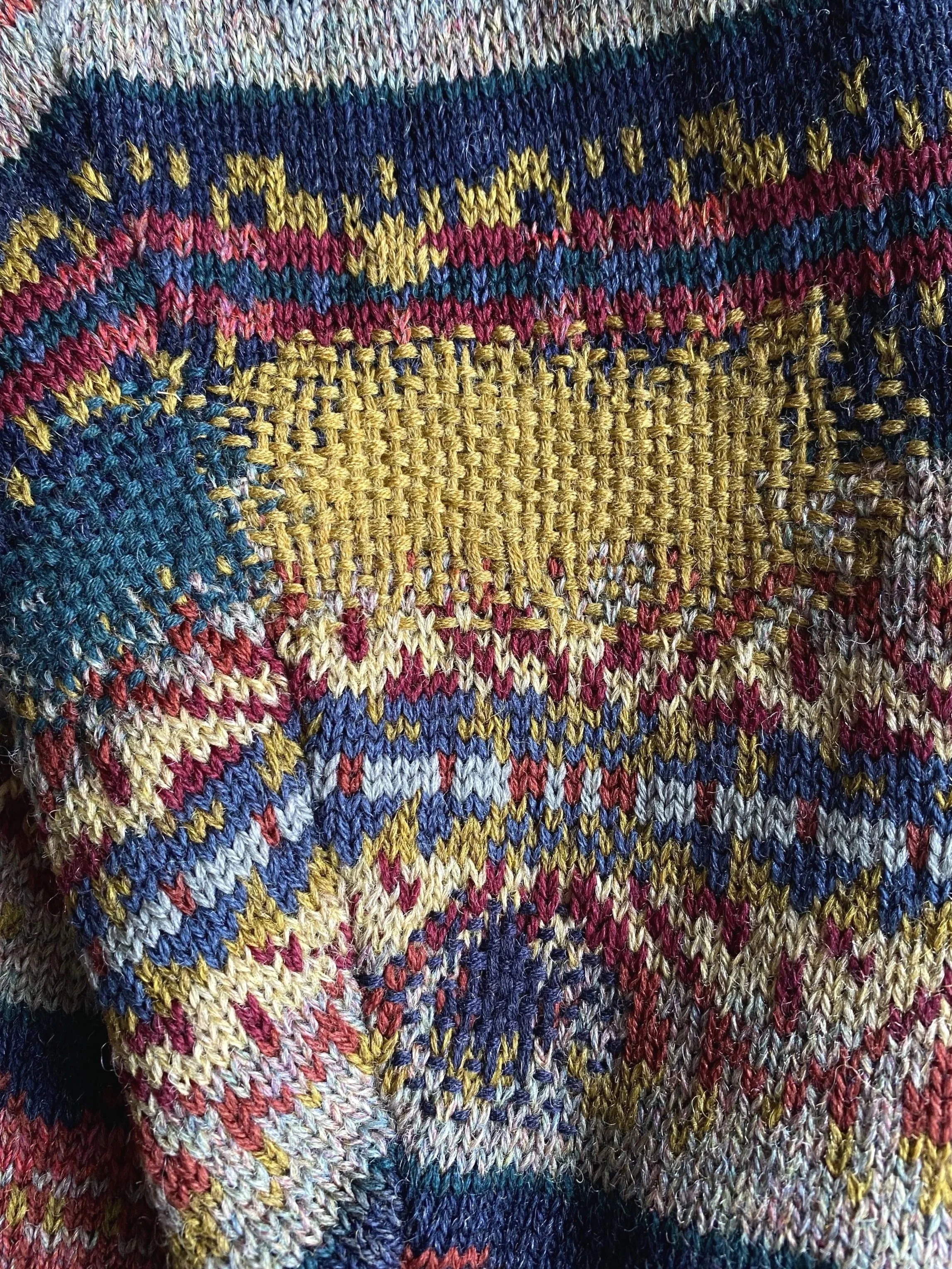 Visibly mended holes in Fair Isle knit cardigan using single colour of yarn per darn using colours from original knit