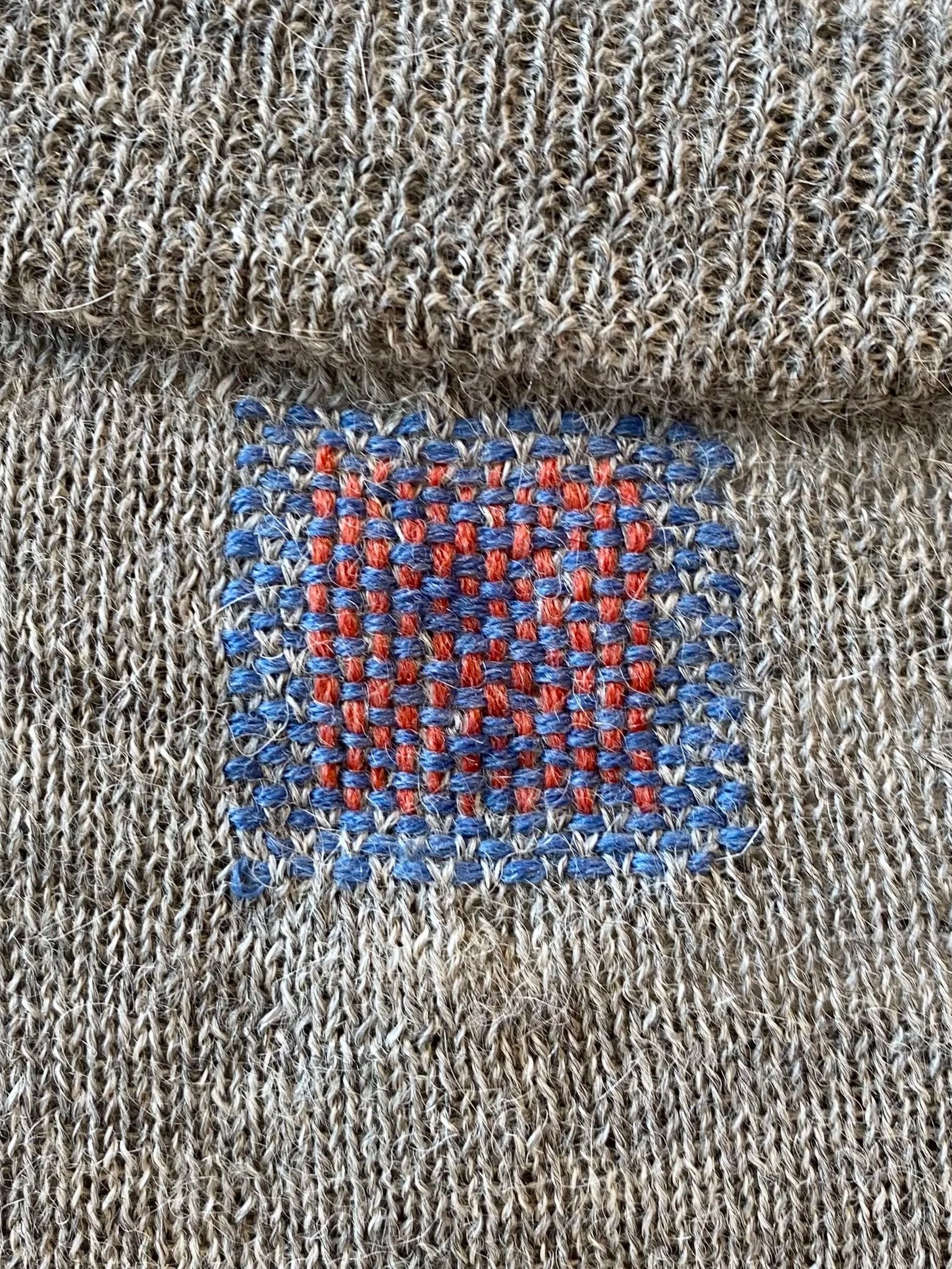 Visible mend on knitwear: Grey knit with light blue horizontal stitching and peach vertical stitching