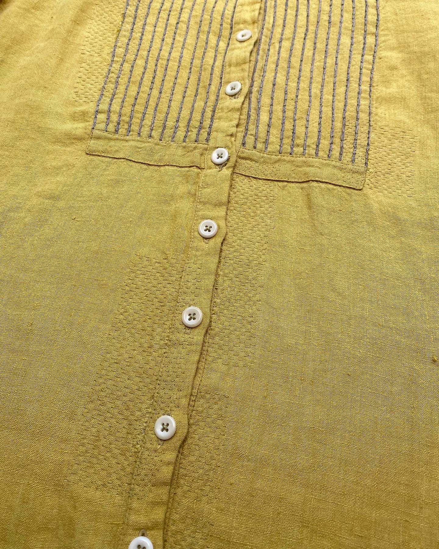 Invisible repair, sashiko style on linen shirt: Yellow linen shirt with the faintest small stitches in various areas alongside the fabric around the buttons.