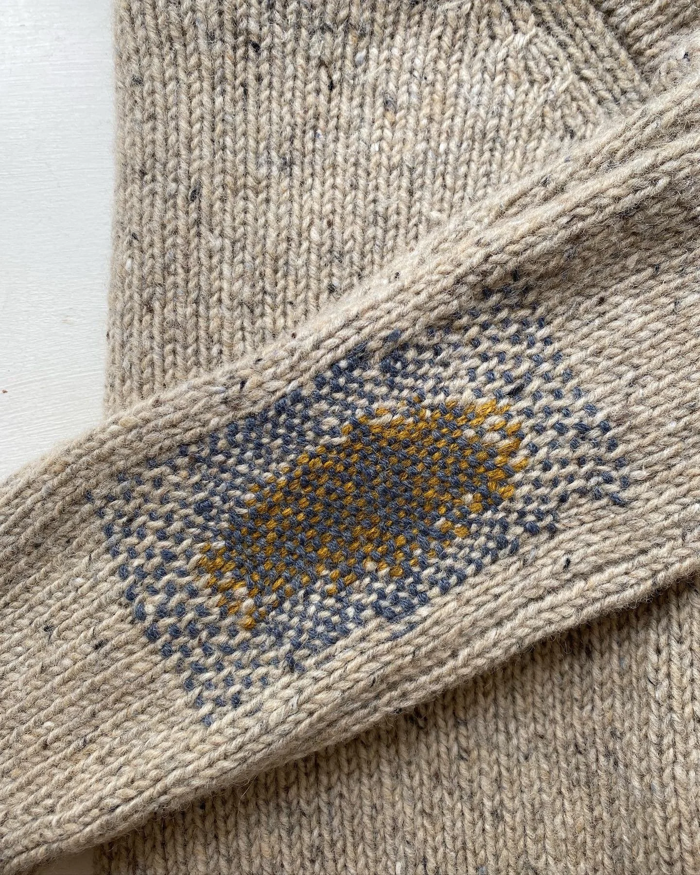 Visible mend on jumper elbow in mustard and grey yarn on flecked cream wool