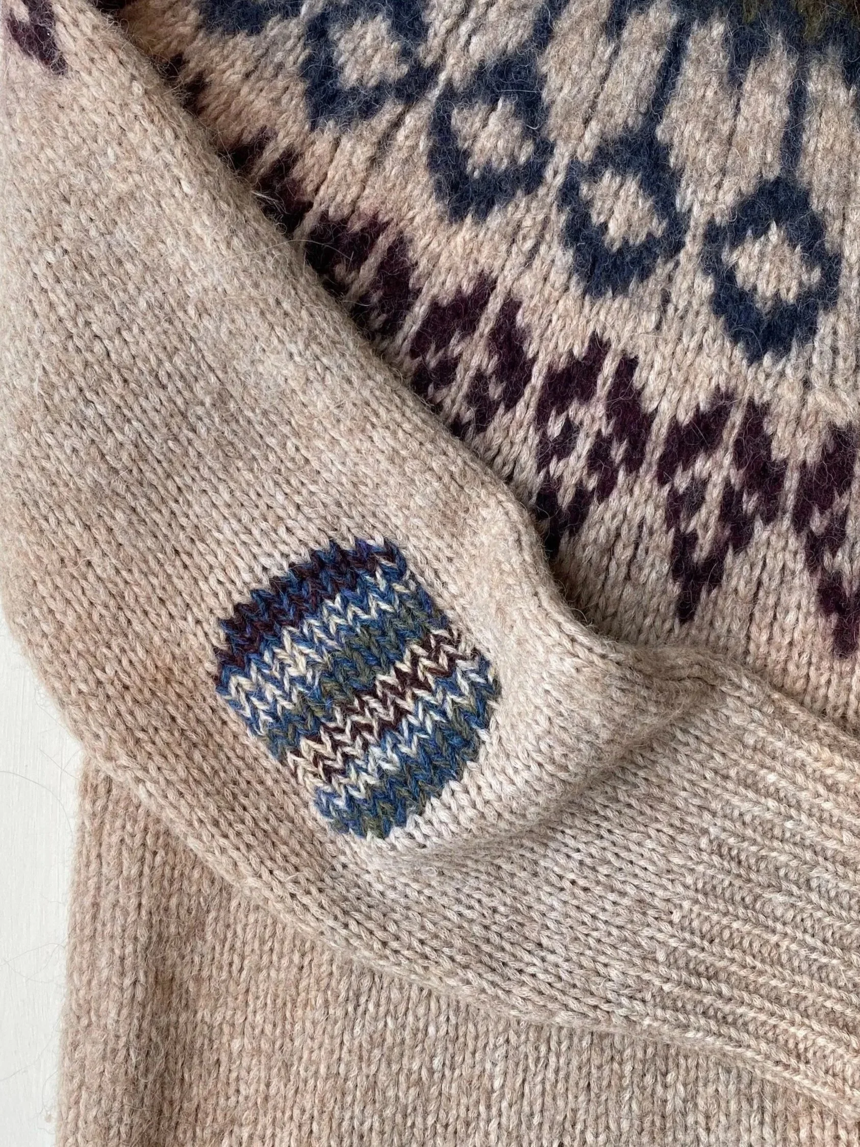 Visible mend on elbow of jumper: Elbow repaired using a Swiss darn or duplicate stitch in a mix of colours matching the jumper's fair-isle pattern.