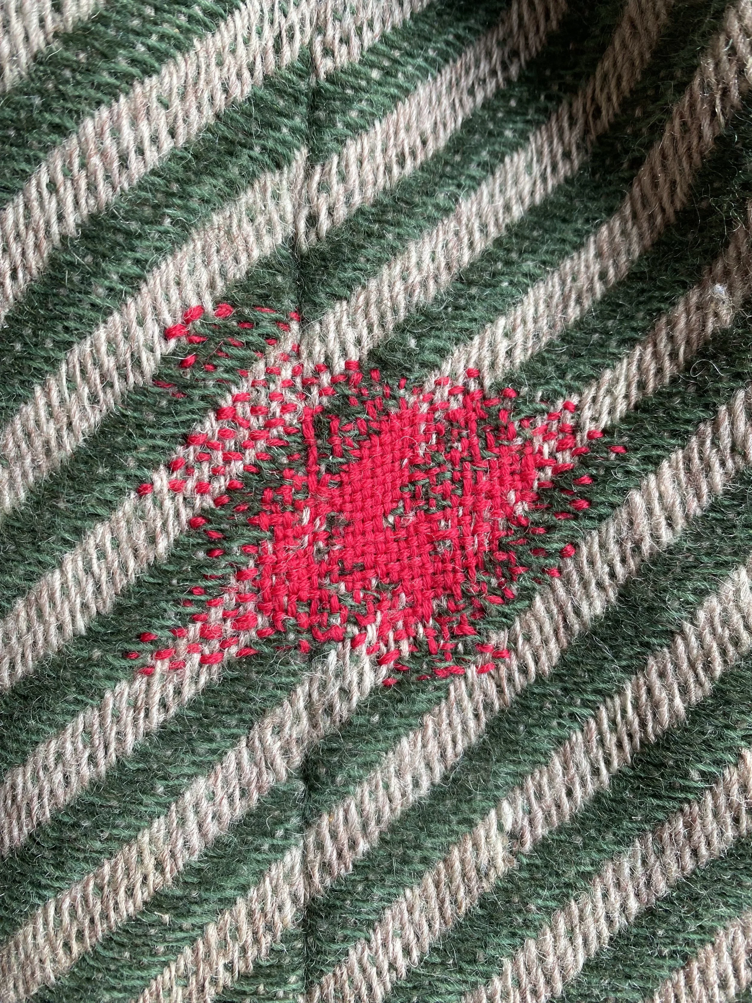 Visible darn on woven wool coat: Bright pink yarn woven and darned area of green and beige diagonal stripe wool coat.