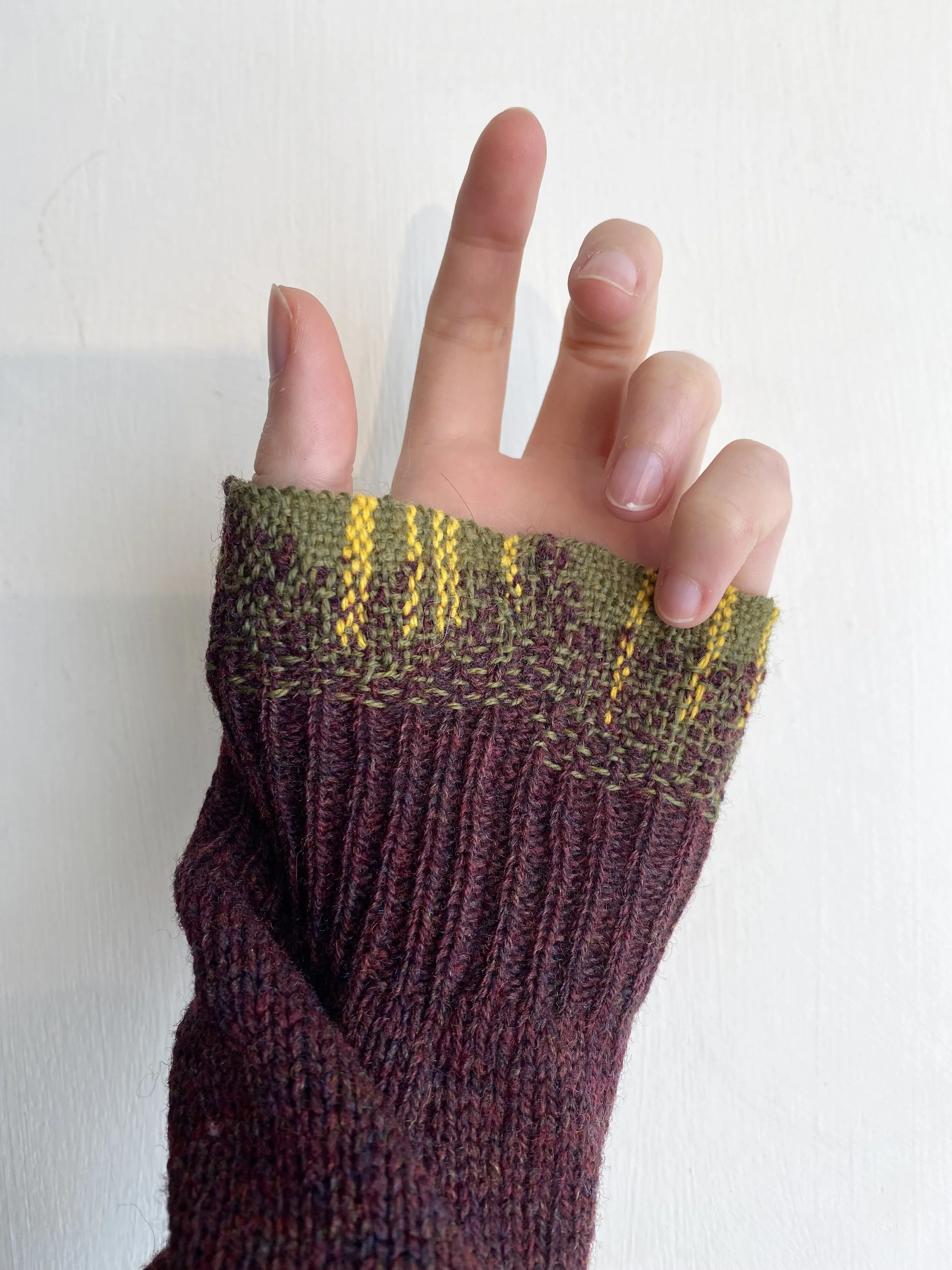 Visible mend on knitwear cuff: Burgundy knitted sleeve with woven darn in khaki green with some lines of bright yellow