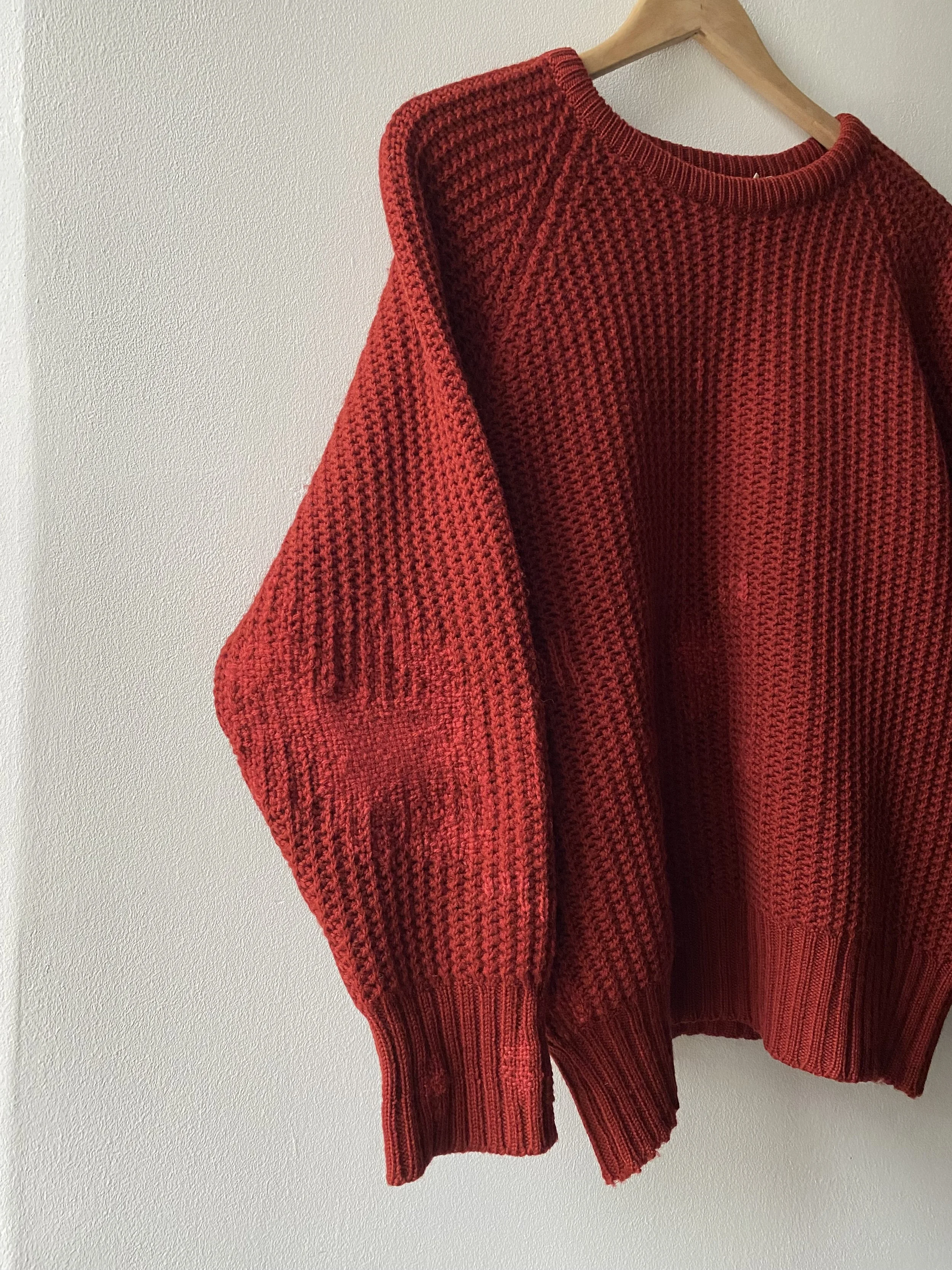Discreet repair using woven darning on red wool jumper: Bold red ribbed knit jumper, woven darns just visible on the sleeve.