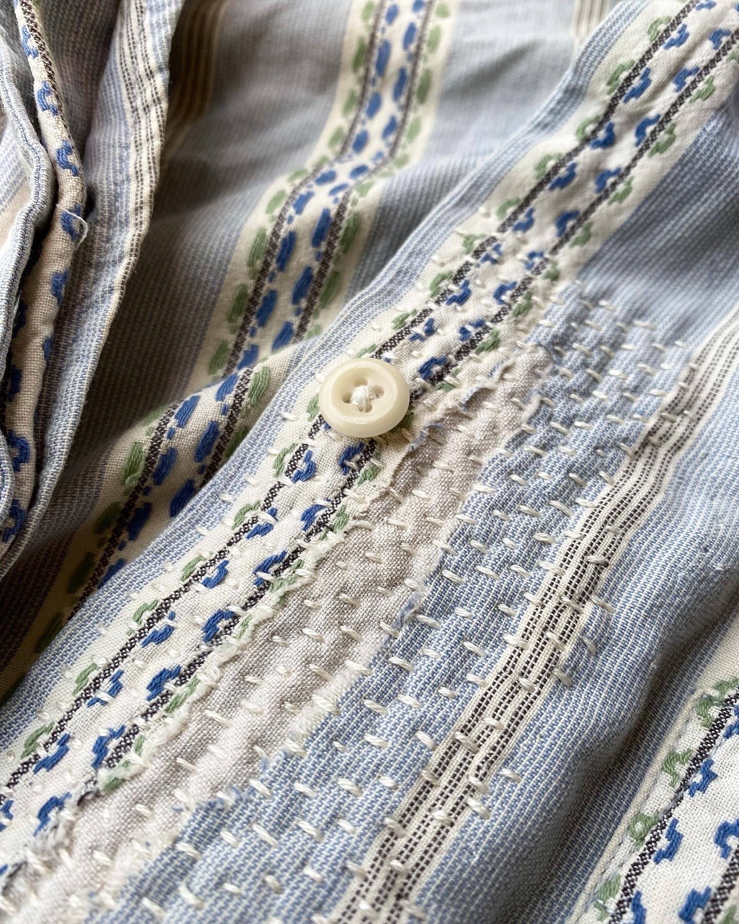 Discreet sashiko patch repair on night shirt. Light blue patterned pyjamas torn near the button placket, patched with cream fabric on the inside and stitched on top horizontally with cream thread.