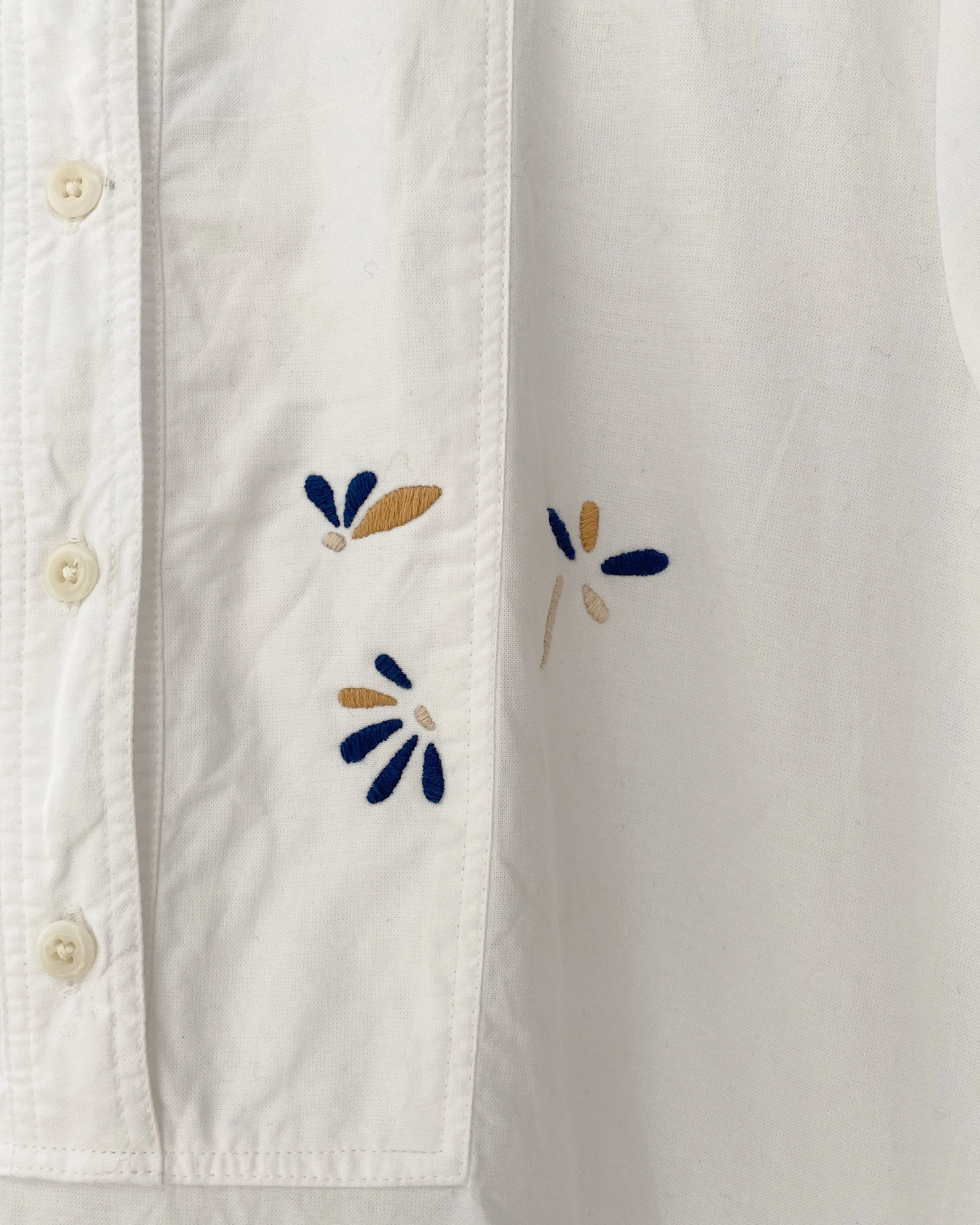Visible mend on white cotton dress: Hand embroidery to cover pen marks on white cotton dress, floral embroidery in navy, mustard and cream threads.