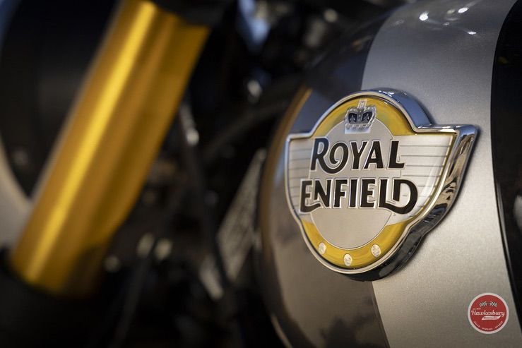 Close-up of a motorcycle's fuel tank with a Royal Enfield badge and a yellow front fork visible.