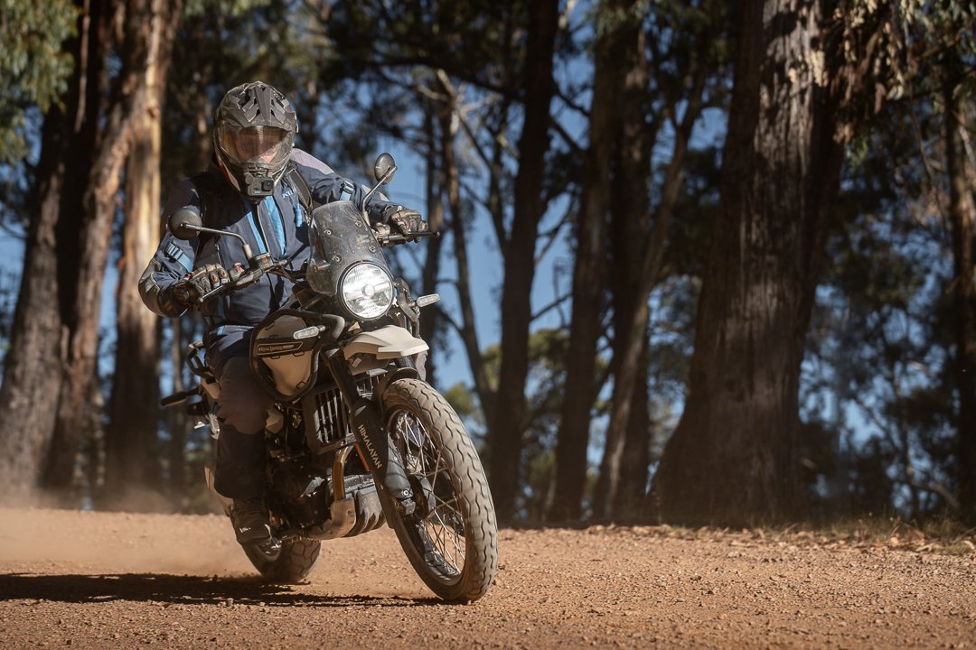 A person riding a dual-sport motorcycle on a dirt trail through a wooded area.