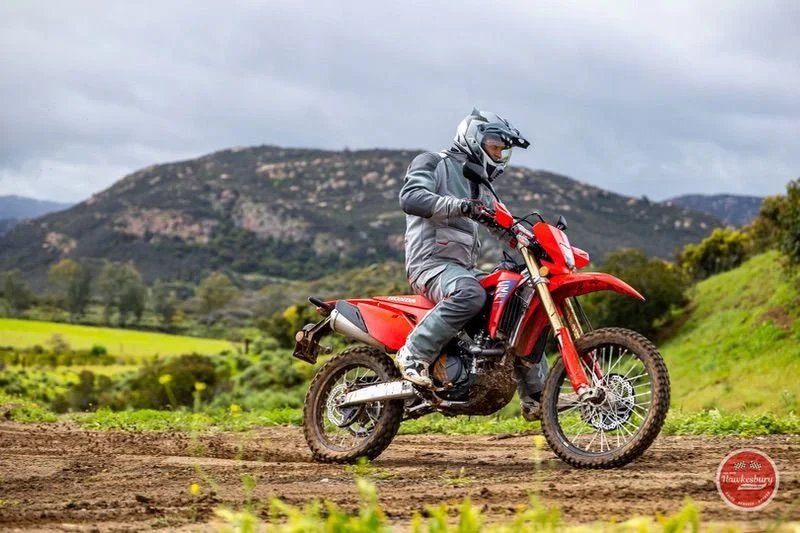 Motorcycle rider in helmet and protective gear riding on dirt trail with green fields and mountains in the background