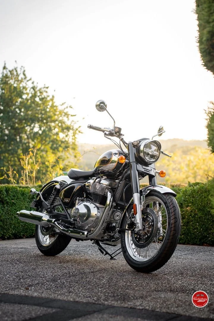 A black and chrome motorcycle parked on a driveway with greenery and trees in the background during sunset.