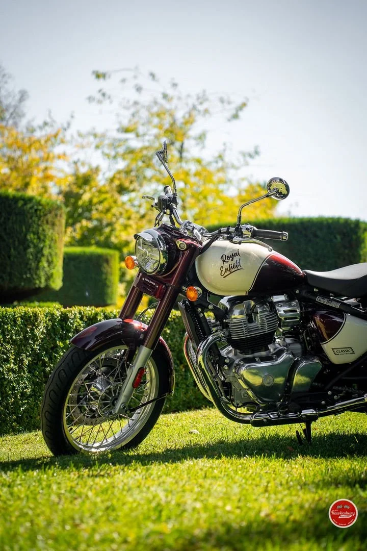 A Royal Enfield motorcycle parked on a grassy area with neatly trimmed bushes and trees in the background.