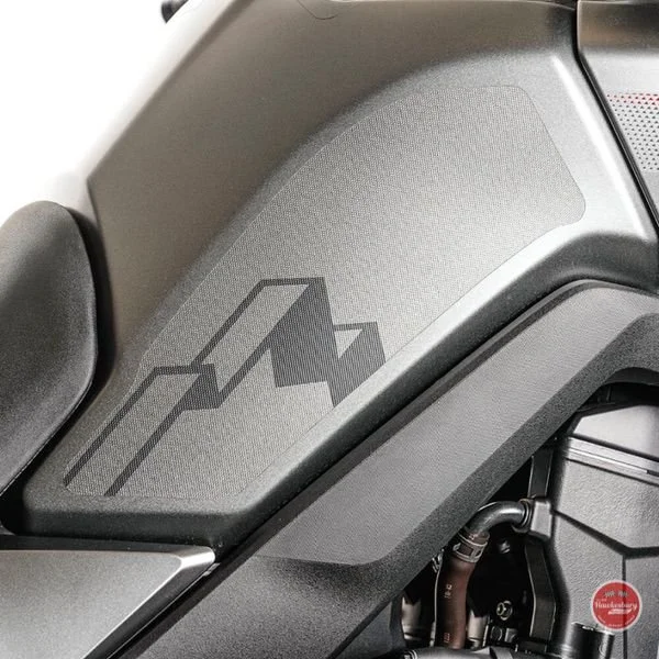 Close-up of a gray motorcycle side panel with a logo resembling a stylized mountain peak.
