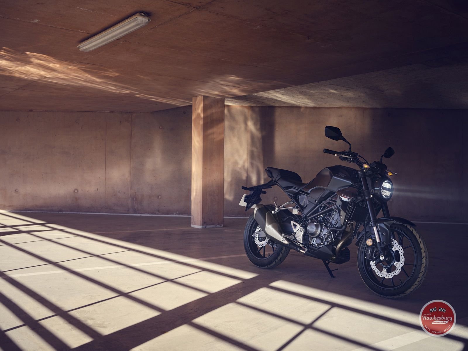 A black motorcycle parked inside a concrete parking garage with sunlight casting shadows through a window.