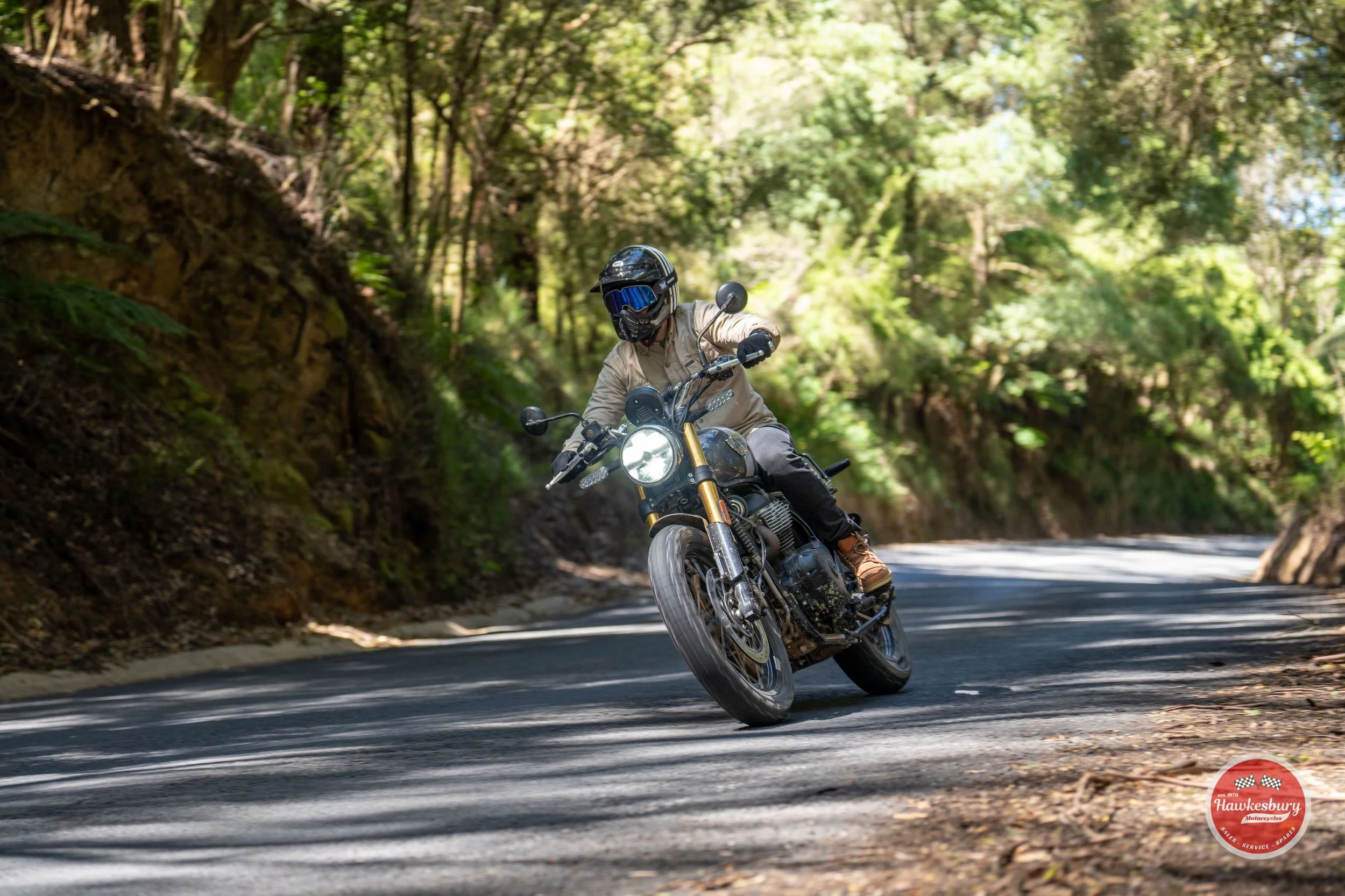 Motorcyclist in black helmet and sunglasses riding on a winding forested road during daytime.