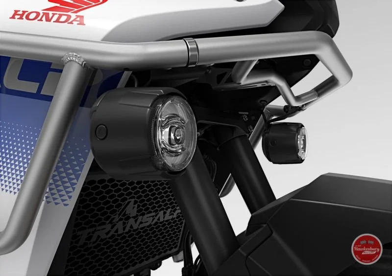 Close-up of a Honda motorcycle front section showing headlights, black suspension forks, and part of the Honda logo.