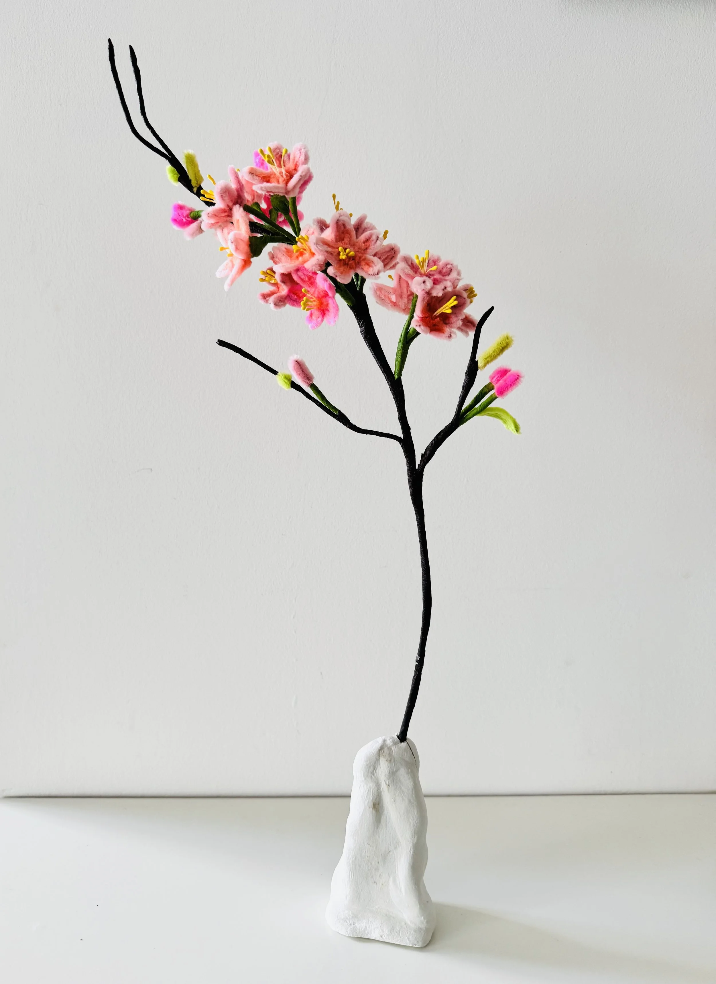 Pipe cleaners flower arrangement with pink blossoms, green leaves, and black stems on a white base.