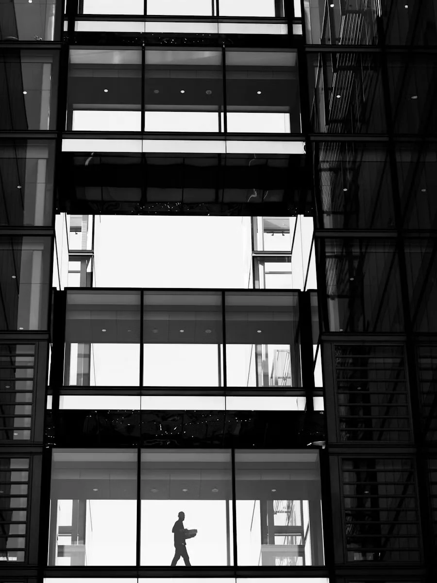 Silhouette of a person walking inside a modern building with glass walls and multiple floors.
