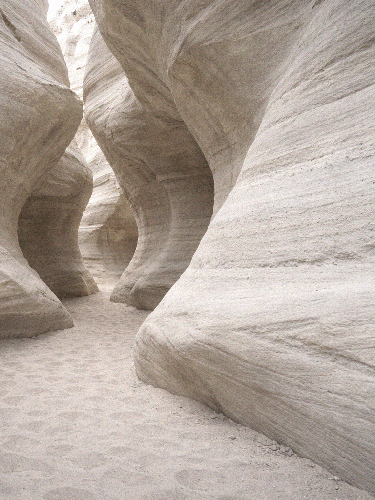 Narrow canyon with smooth, layered sandstone walls and sandy floor