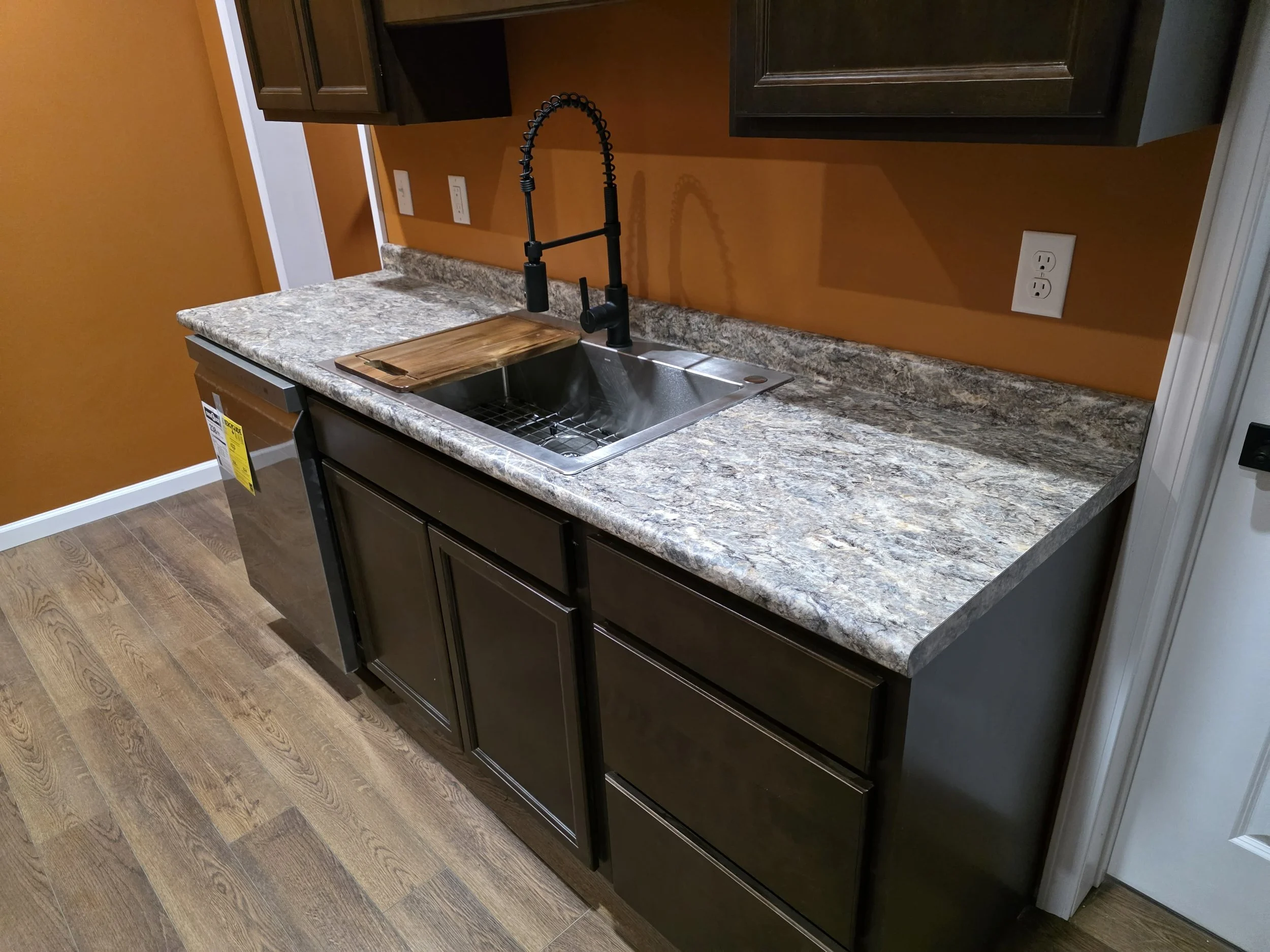 Kitchen countertop with a stainless steel sink, black pull-down faucet, wooden cutting board, dark brown cabinets, We serve homeowners and businesses in Madison, Hanover, Scottsburg, Austin, Milton, KY, Carrollton, KY and surrounding communities 