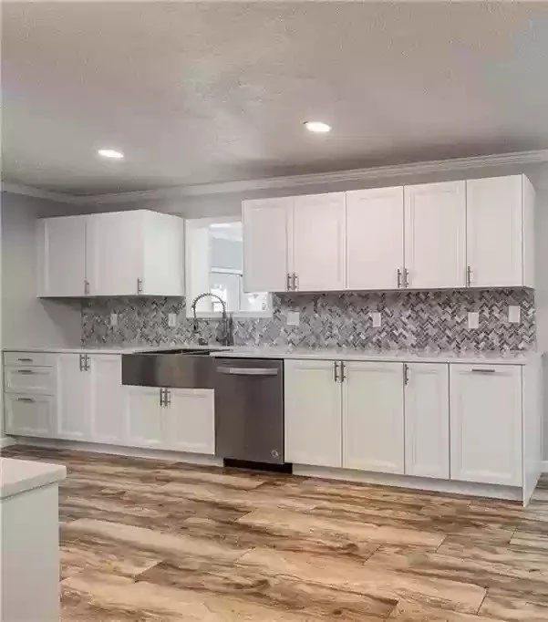 Modern kitchen with white cabinets, a stainless steel sink and dishwasher, a patterned tile backsplash, and wood-look flooring. We serve homeowners and businesses in Madison, Hanover, Scottsburg, Austin, Milton, KY, Carrollton, KY and surrounding