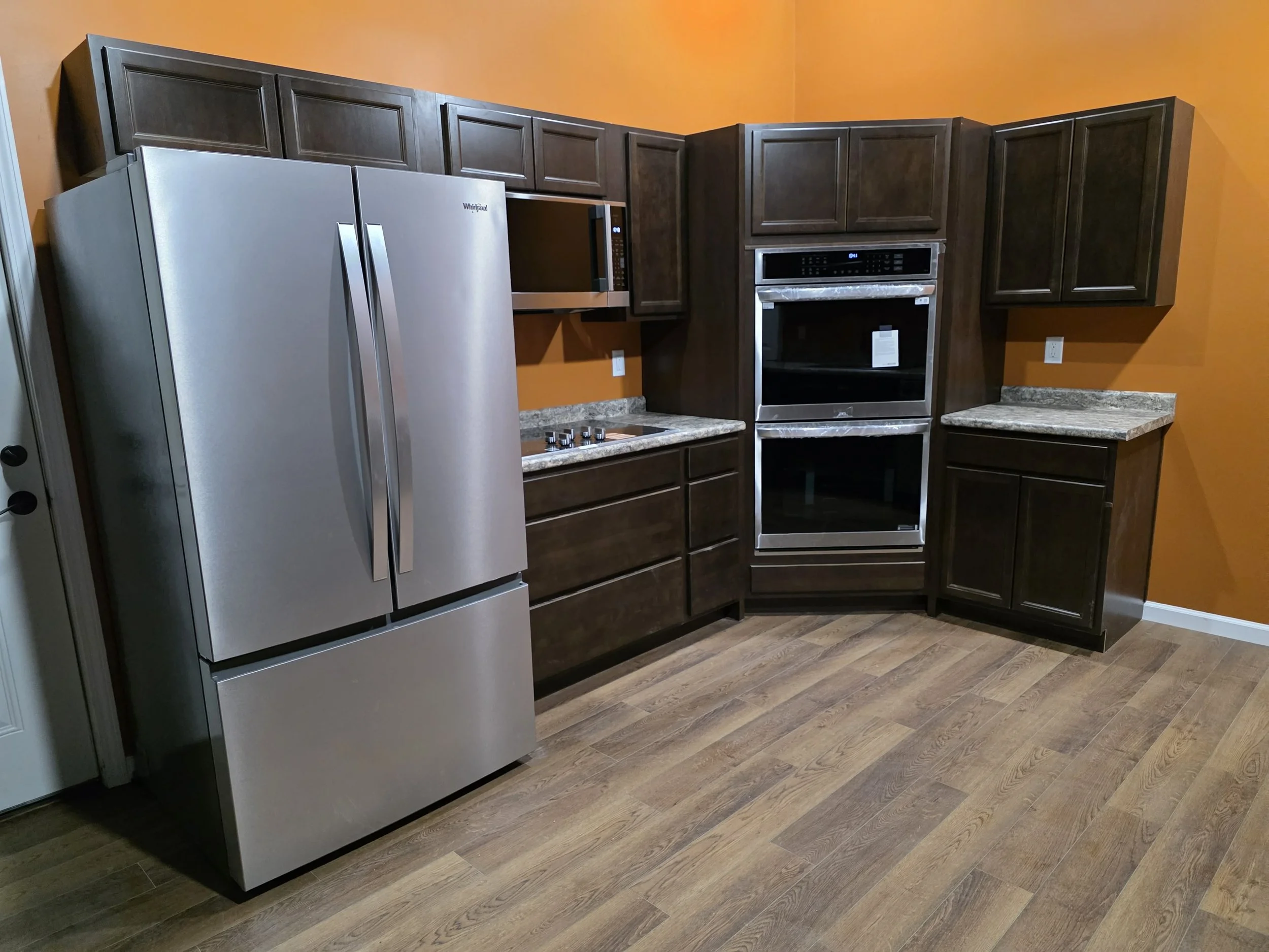 Modern kitchen with orange walls, dark brown cabinets, stainless steel refrigerator, microwave, double oven, and granite countertops. We serve homeowners and businesses in Madison, Hanover, Scottsburg, Austin, Milton, KY, Carrollton, KY