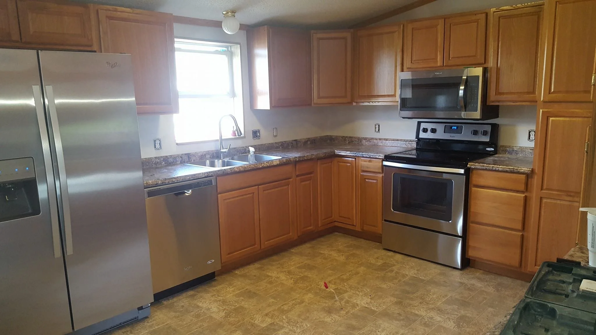 Kitchen with wooden cabinets, stainless steel refrigerator, dishwasher, oven, and microwave. Granite countertops, double sink under window, We serve homeowners and businesses in Madison, Hanover, Scottsburg, Austin, Milton, KY, Carrollton, KY