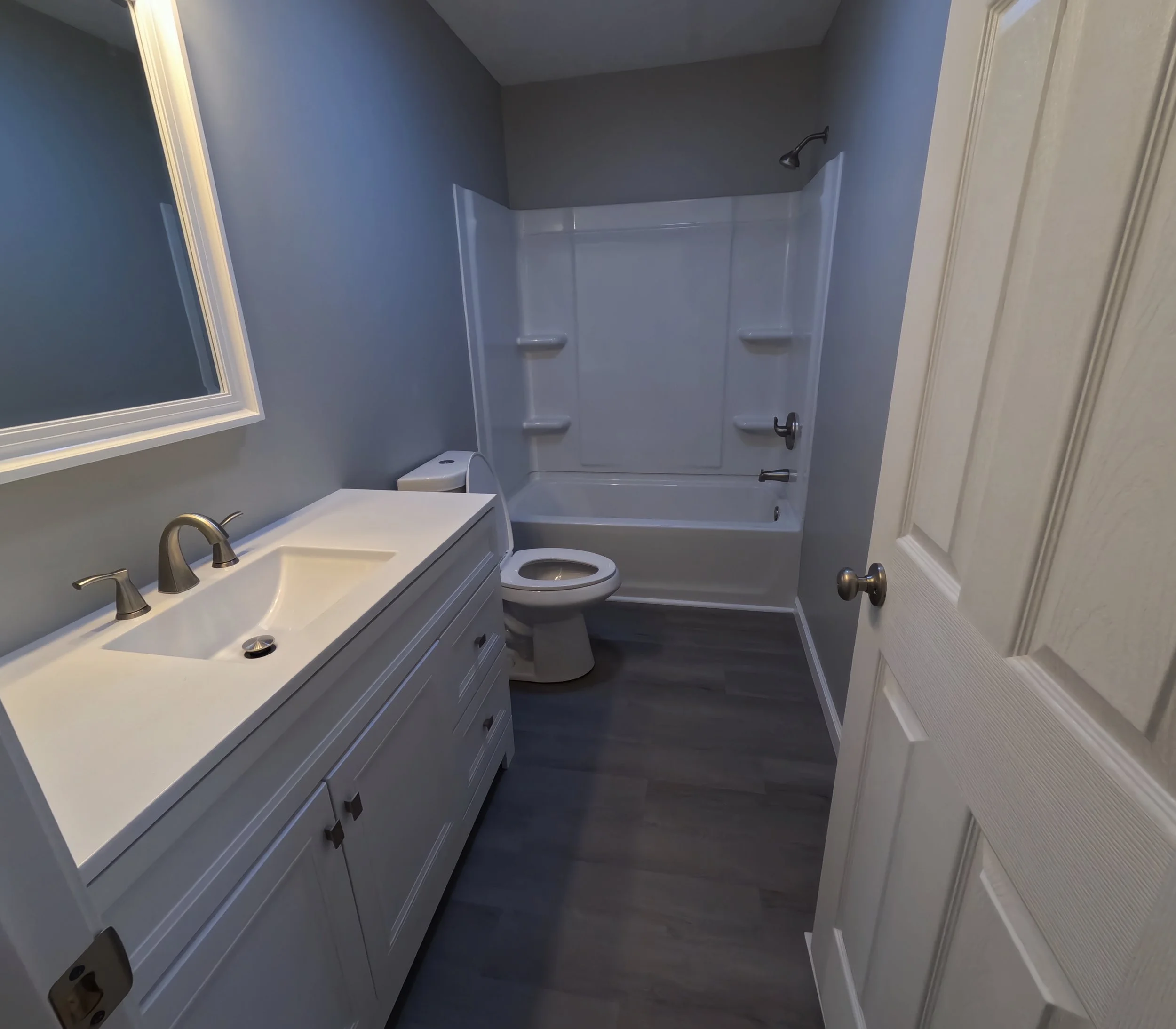 Small bathroom with gray walls, white vanity with a sink, mirror, toilet, and a bathtub with a shower. We serve homeowners and businesses in Madison, Hanover, Scottsburg, Austin, Milton, KY, Carrollton, KY and surrounding communities throughout