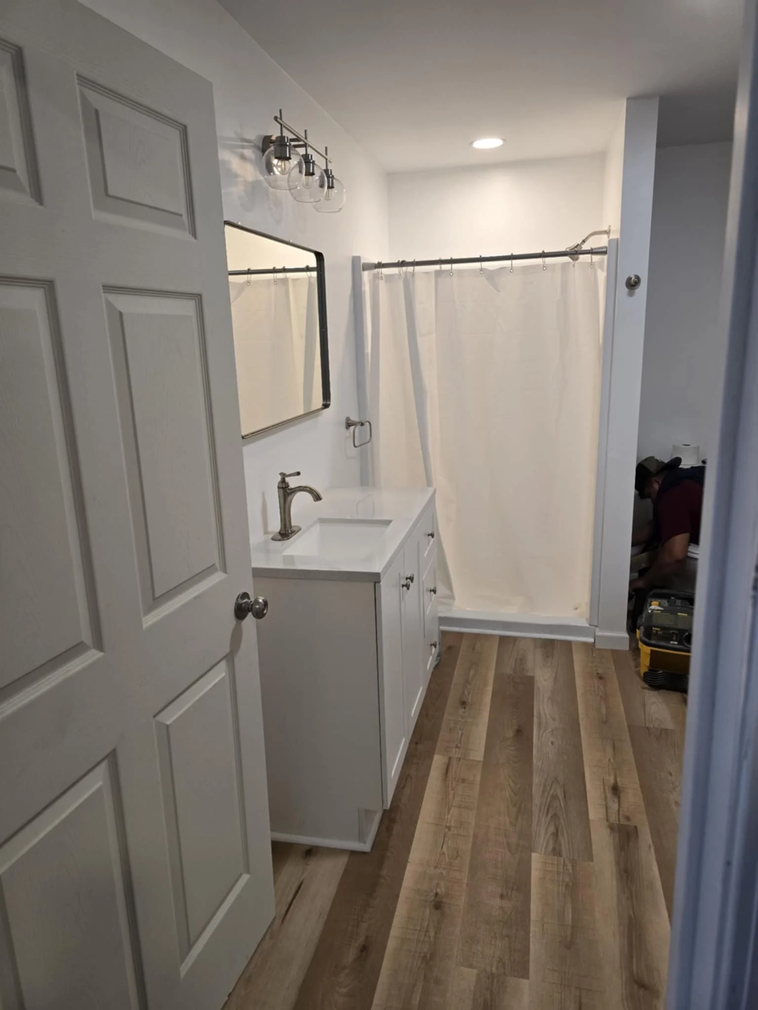 Modern bathroom with white vanity, rectangular mirror, and shower with white curtain. We serve homeowners and businesses in Madison, Hanover, Scottsburg, Austin, Milton, KY, Carrollton, KY and surrounding communities throughout Jefferson County, 
