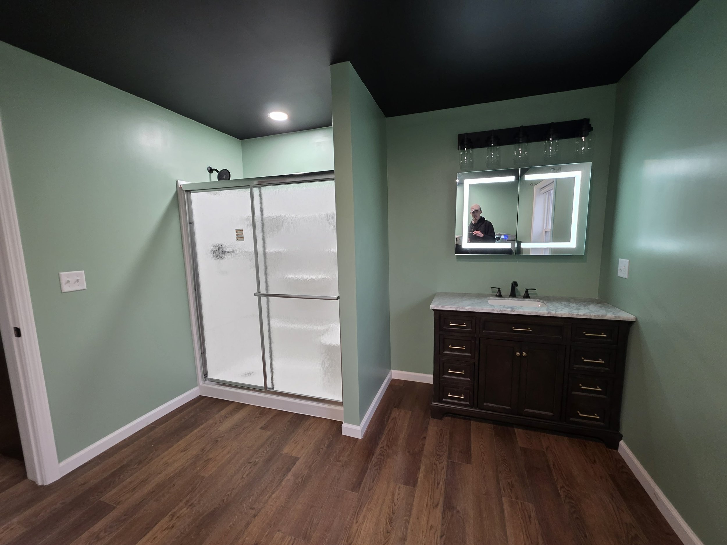 Bathroom with a shower stall, a dark wood vanity with a marble countertop, and a mirror with built-in lighting. We serve homeowners and businesses in Madison, Hanover, Scottsburg, Austin, Milton, KY, Carrollton, KY and surrounding communities