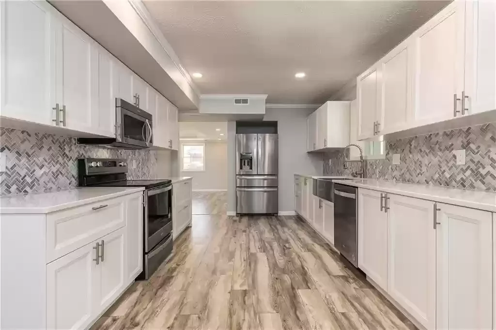 Modern kitchen with white cabinets, stainless steel appliances, a patterned tile backsplash, and wood-look flooring. We serve homeowners and businesses in Madison, Hanover, Scottsburg, Austin, Milton, KY, Carrollton, KY and surrounding communities