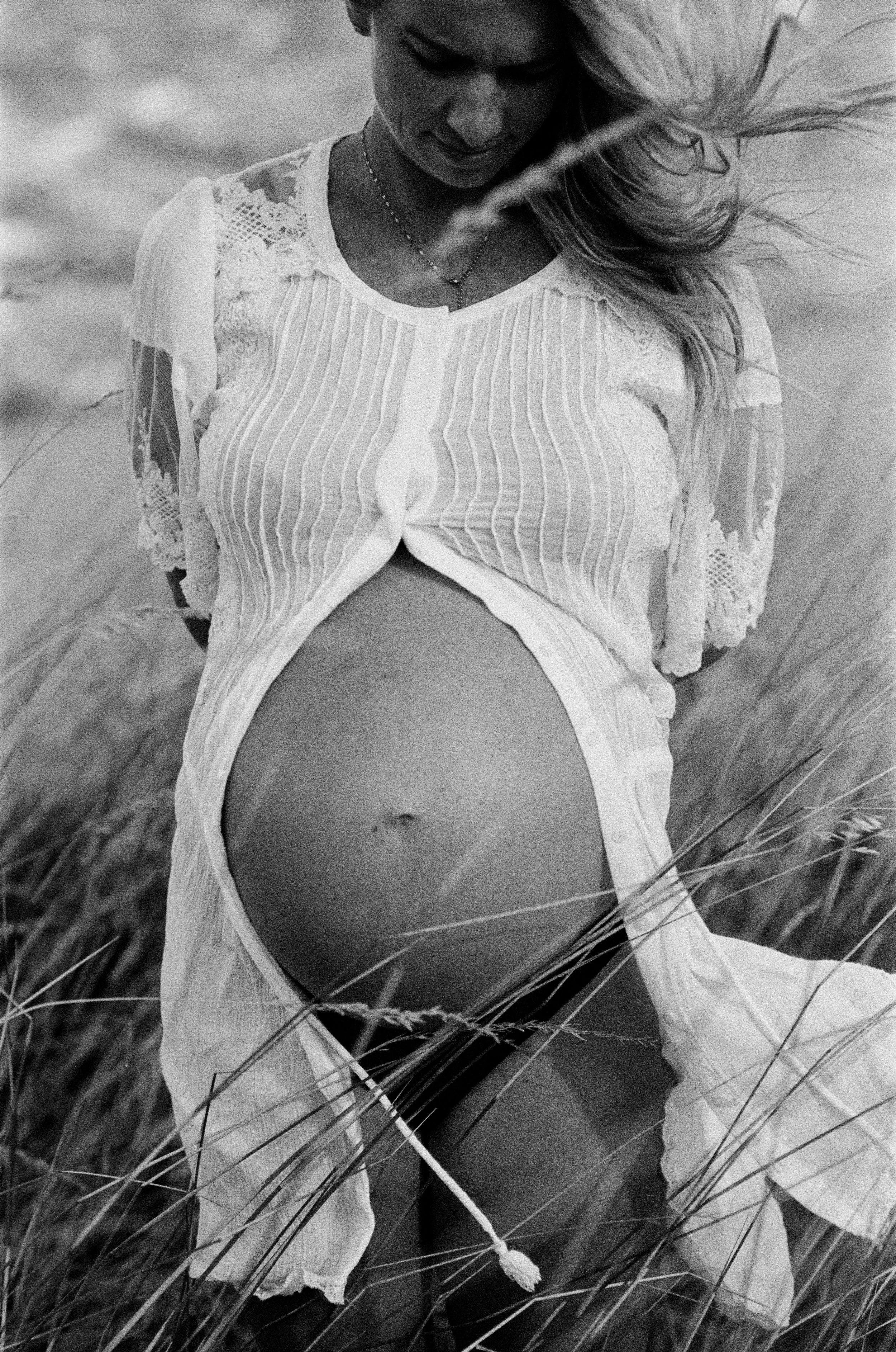 A woman in a lace and striped dress is kneeling in a grassy field, looking down, with her hair blowing to the side.