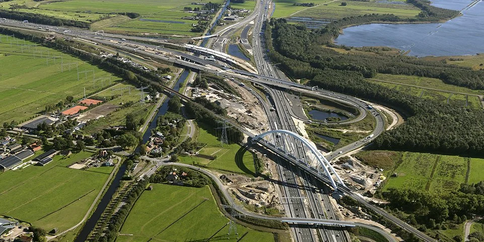 Luchtfoto van snelwegen en bruggen in een groen landschap met waterlichamen en dorpen