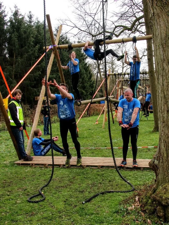 Mensen die een klimparcours tussen bomen doen, met touwen en houten balken.