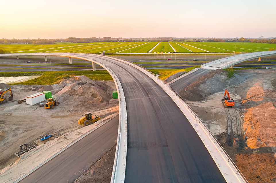 Een toekomstig overspanning op een nieuwe snelweg onder constructie, met oog op landbouwgebieden in de achtergrond.