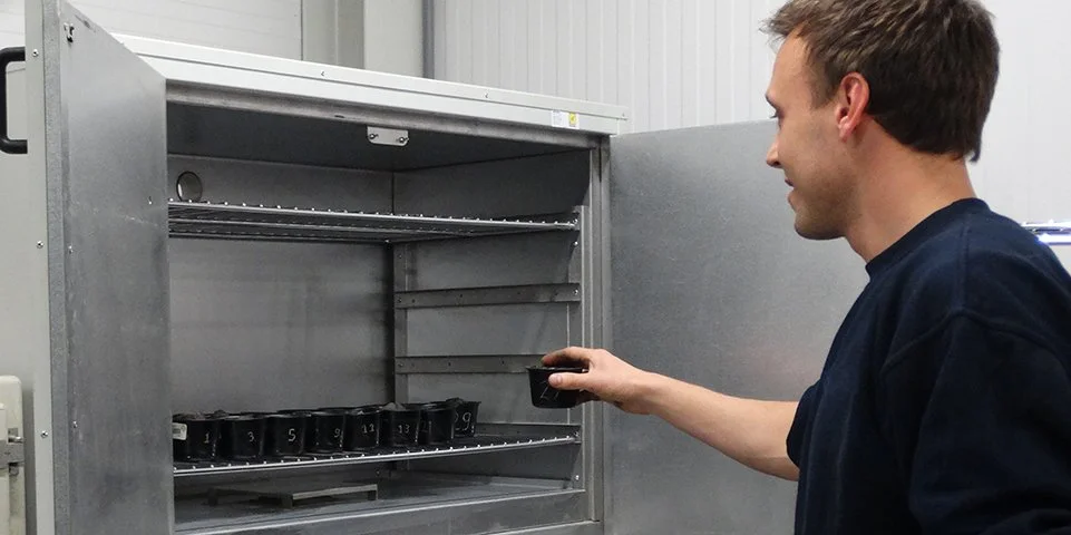 Man plaatst een zwarte kopje in een metalen geventileerde koffiekast.