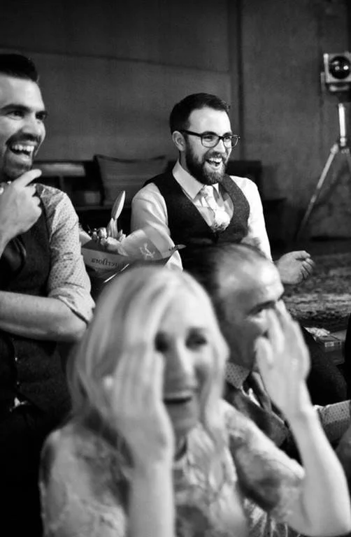 Group of people laughing and enjoying themselves at an indoor event or gathering.